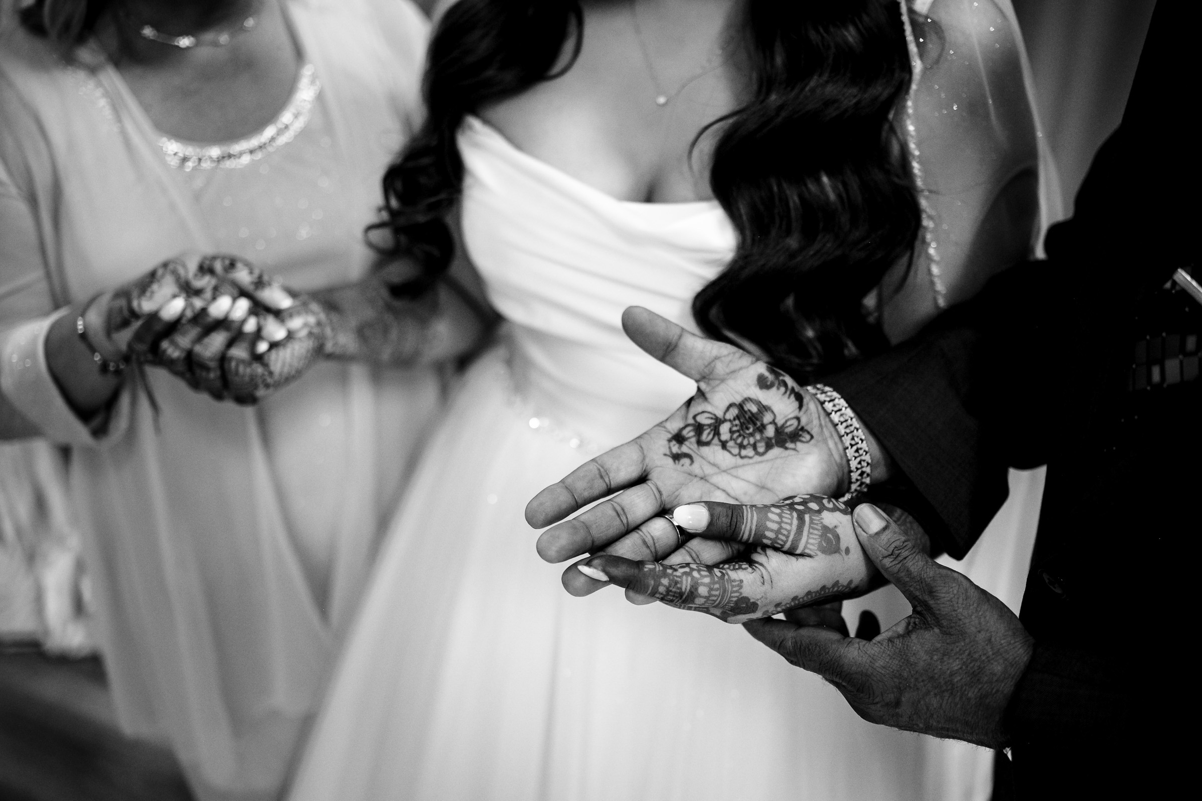 Three people displaying intricate henna designs on their hands during a wedding ceremony.