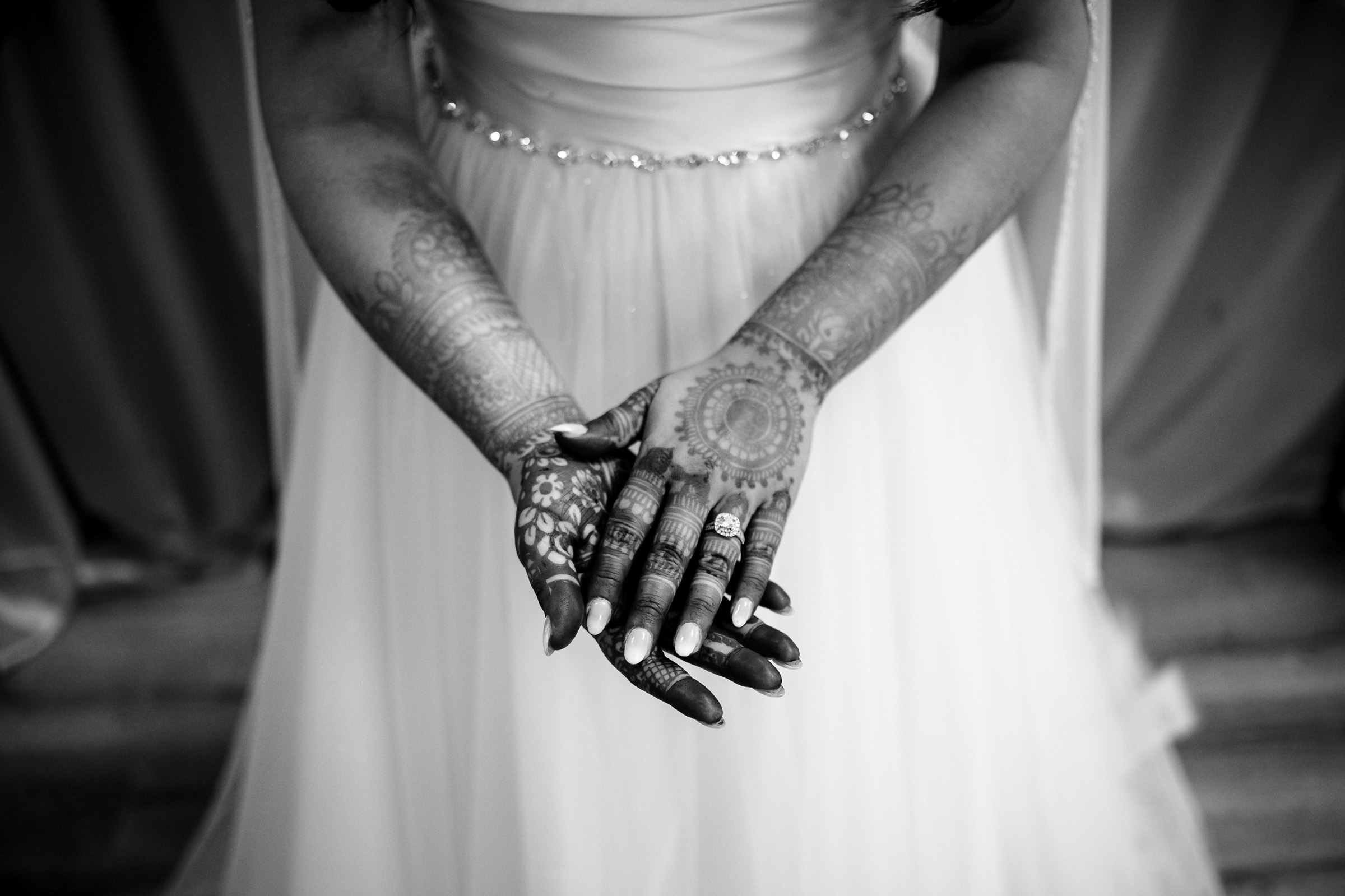 Bride in a white dress with detailed henna on hands, fingers interlocked.
