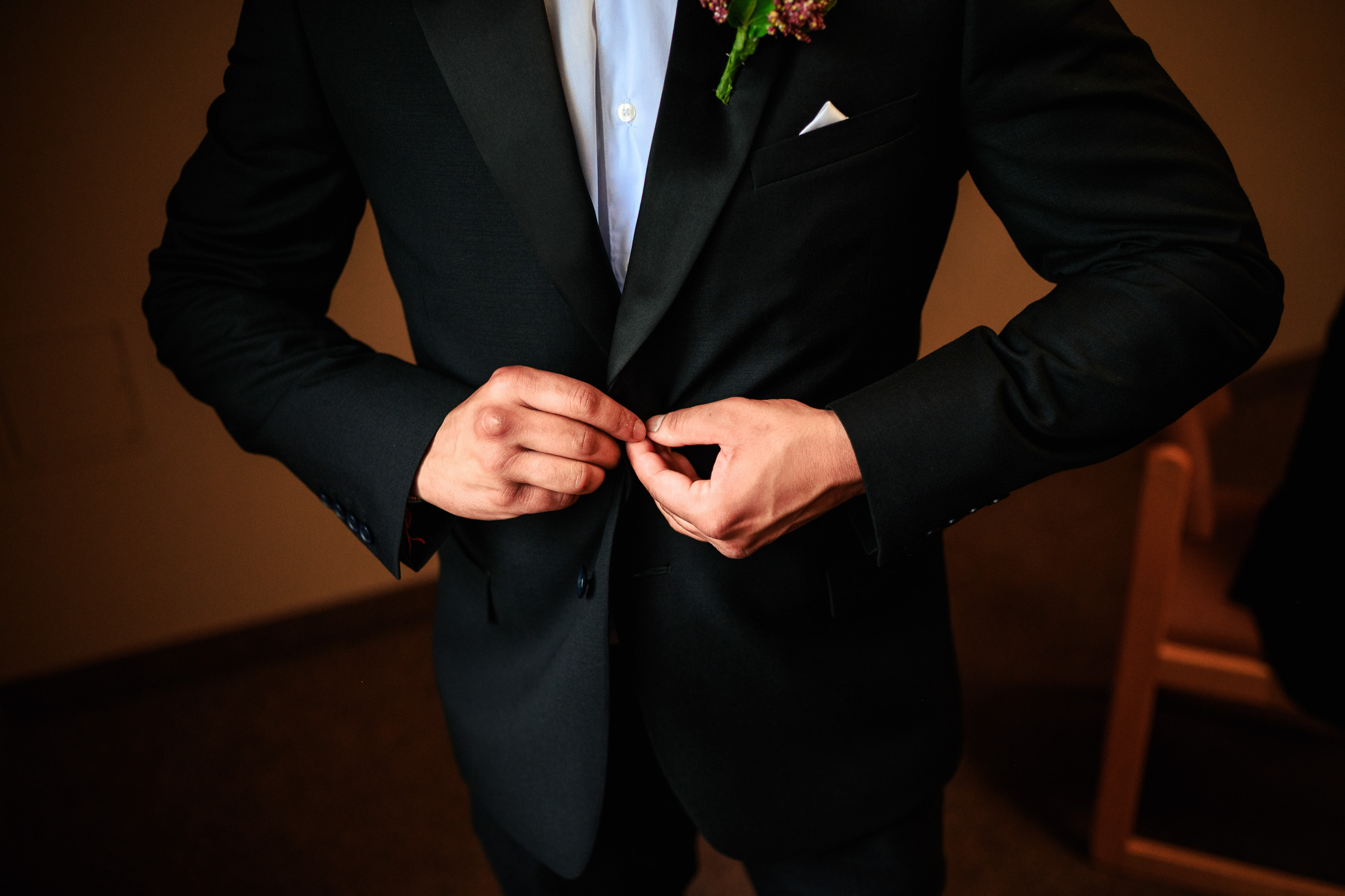 Person buttoning a black suit jacket over a white shirt.