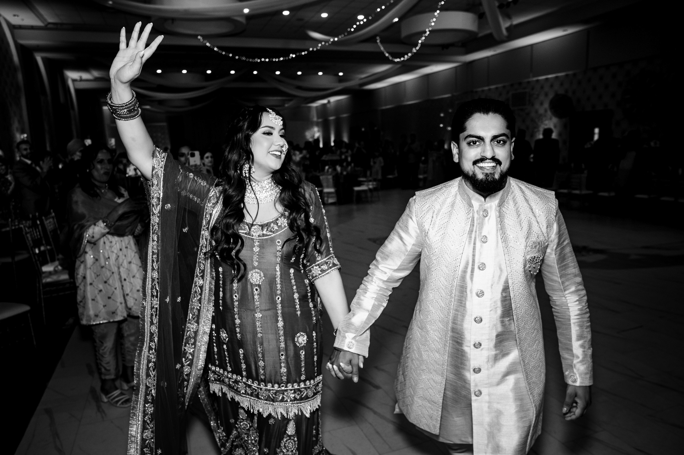 A couple in traditional attire walks hand in hand at an event.