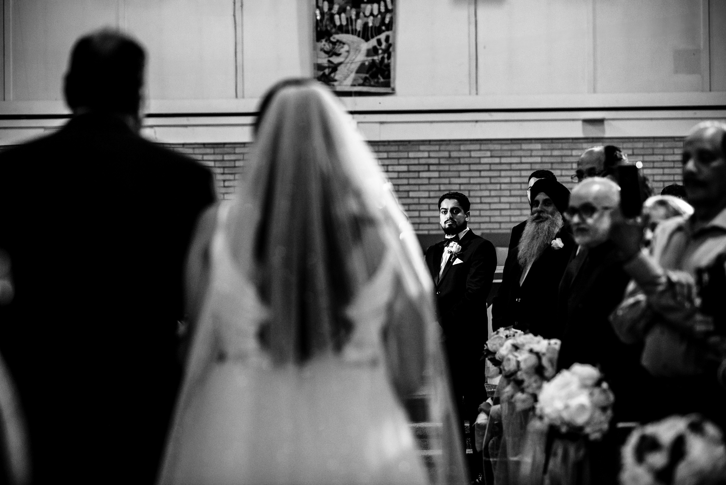 Bride walking down the aisle as groom looks on; guests stand on either side.