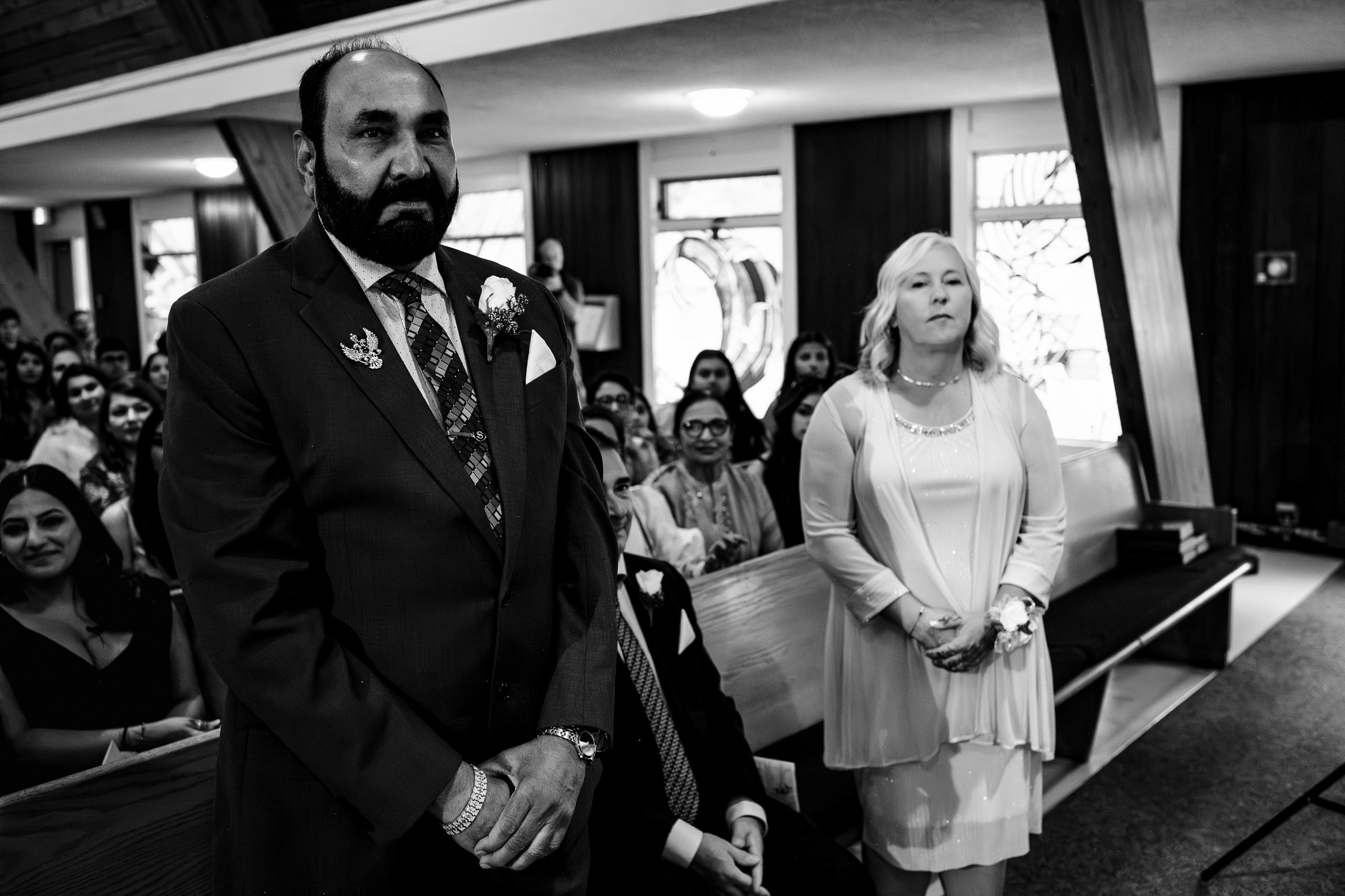 Two people standing at the front of a seated crowd in a room with wooden accents.