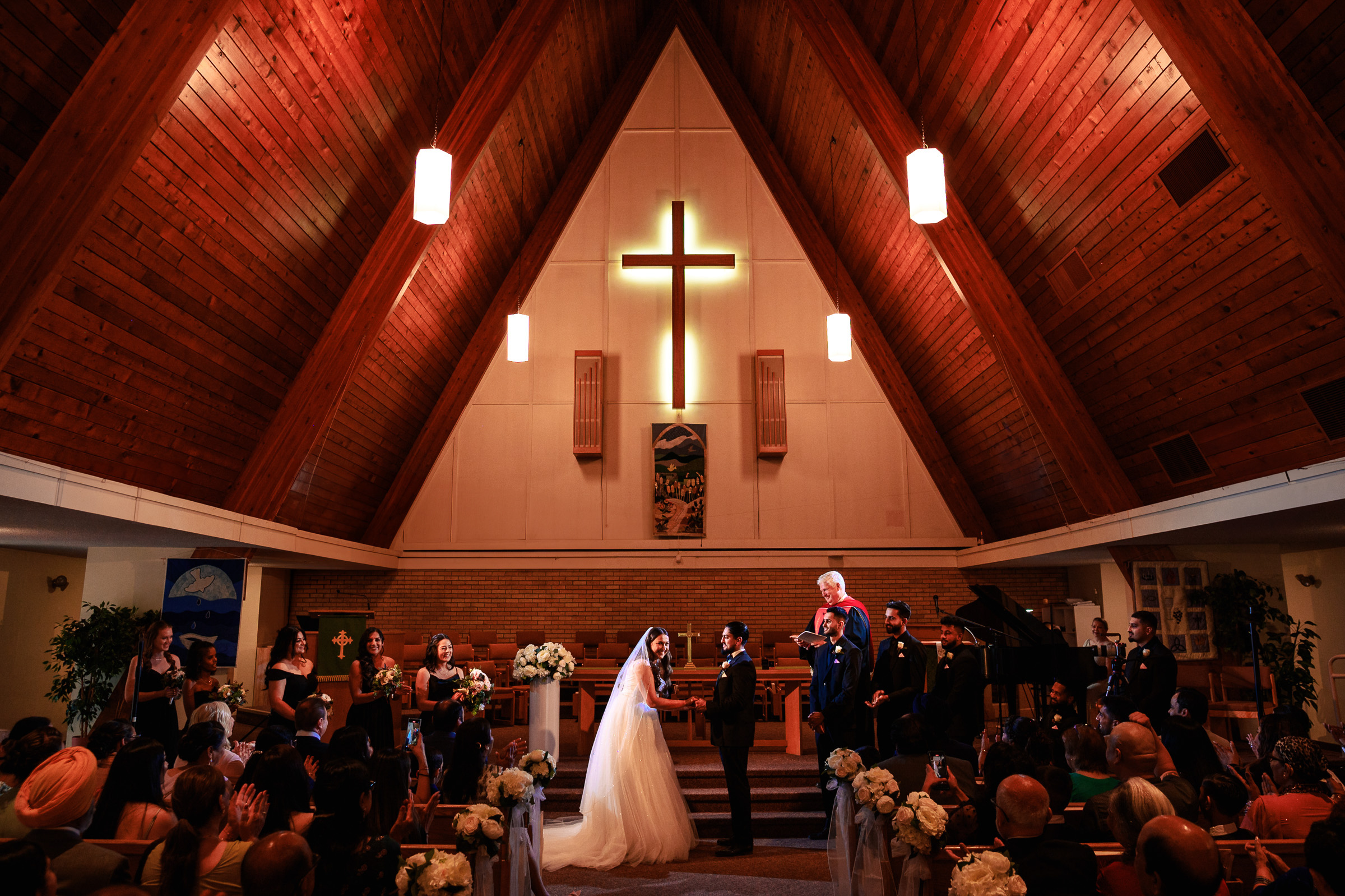 Wedding ceremony in a wooden chapel with a cross, bride and groom holding hands.