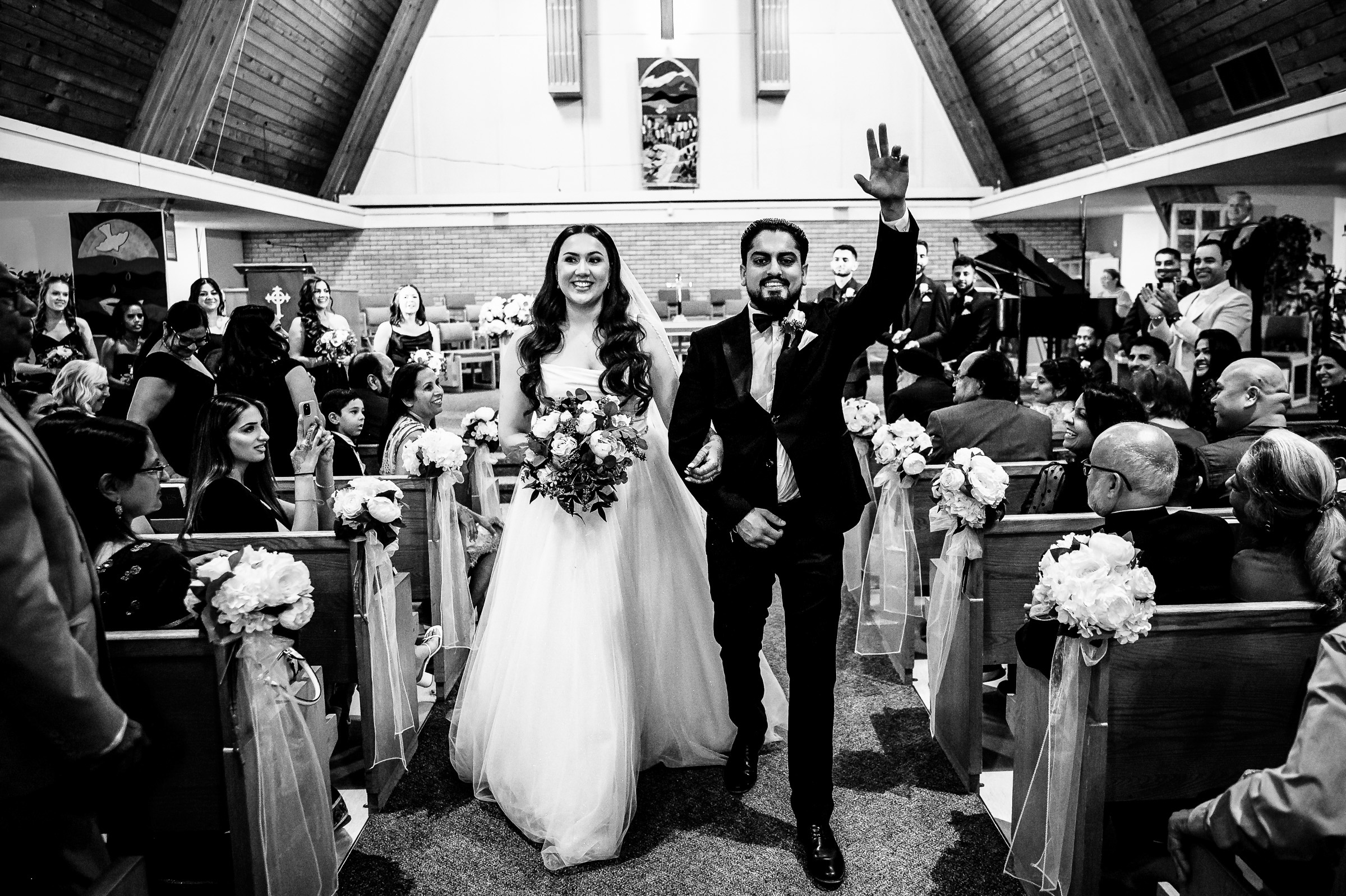 Bride and groom walking down the aisle in a church, with guests seated on either side.