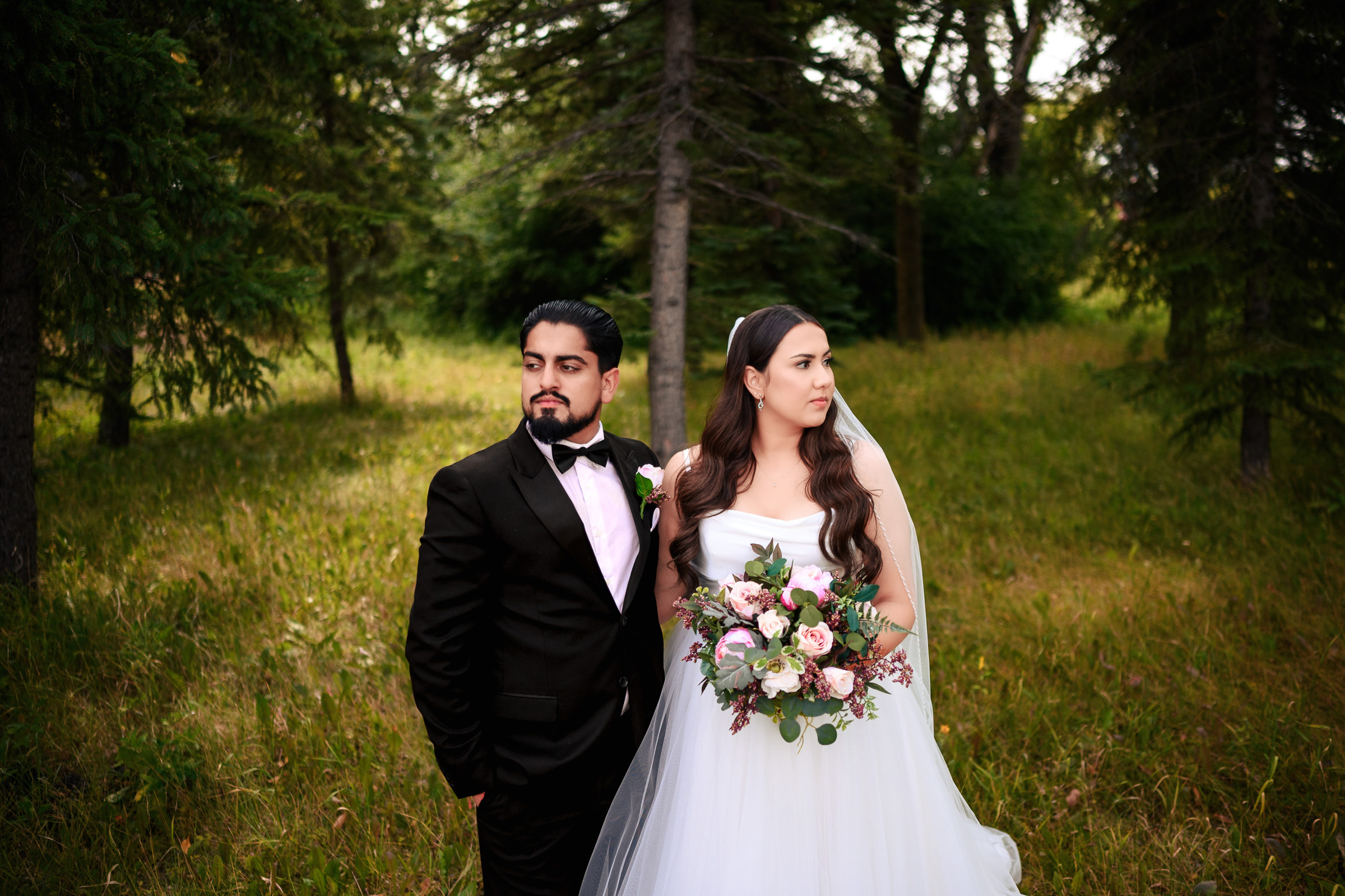 Bride and groom standing together in a forested outdoor setting.