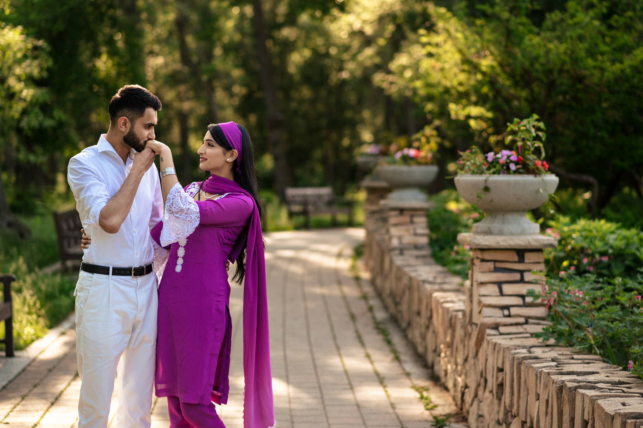 In a home garden, he kisses her hand; she's in purple, he's in white—an intimate engagement.
