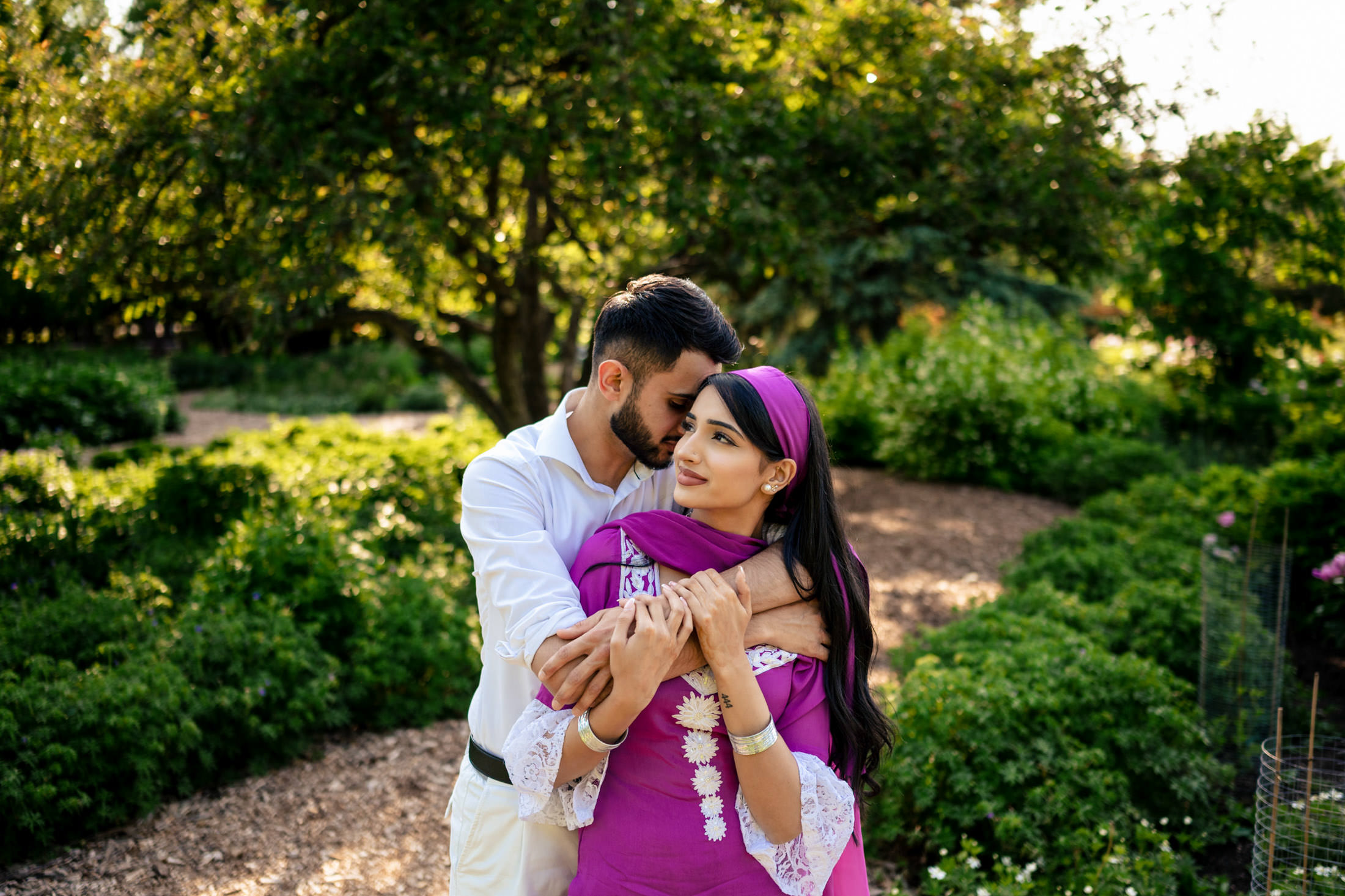 An engaged couple embraces in a serene garden setting.