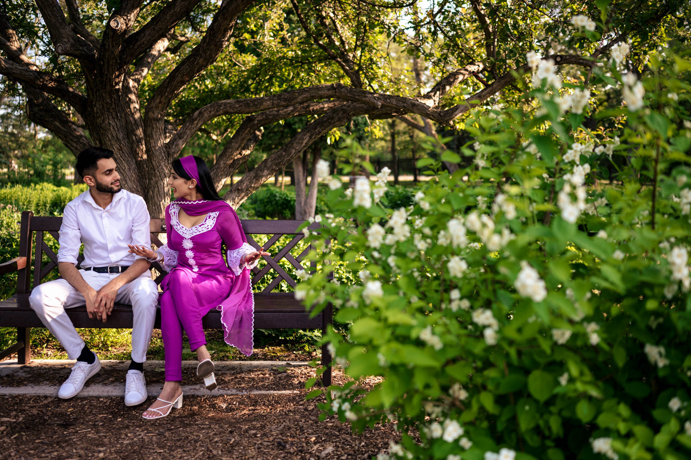Two people sit on a bench in a green park, savoring peaceful moments of engagement.