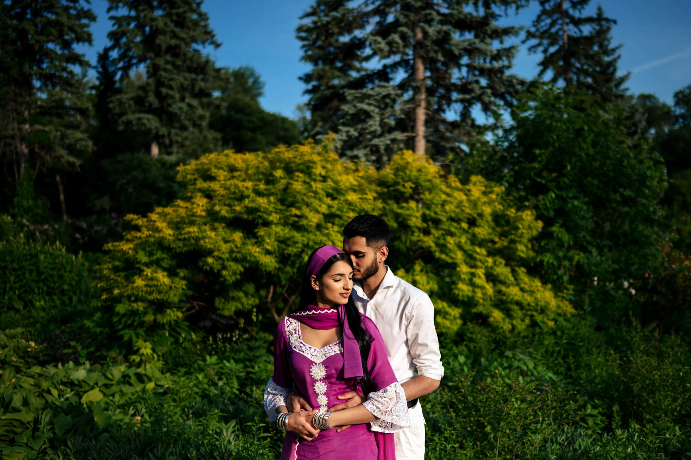 A couple embraces in a vibrant garden, celebrating their engagement at home.