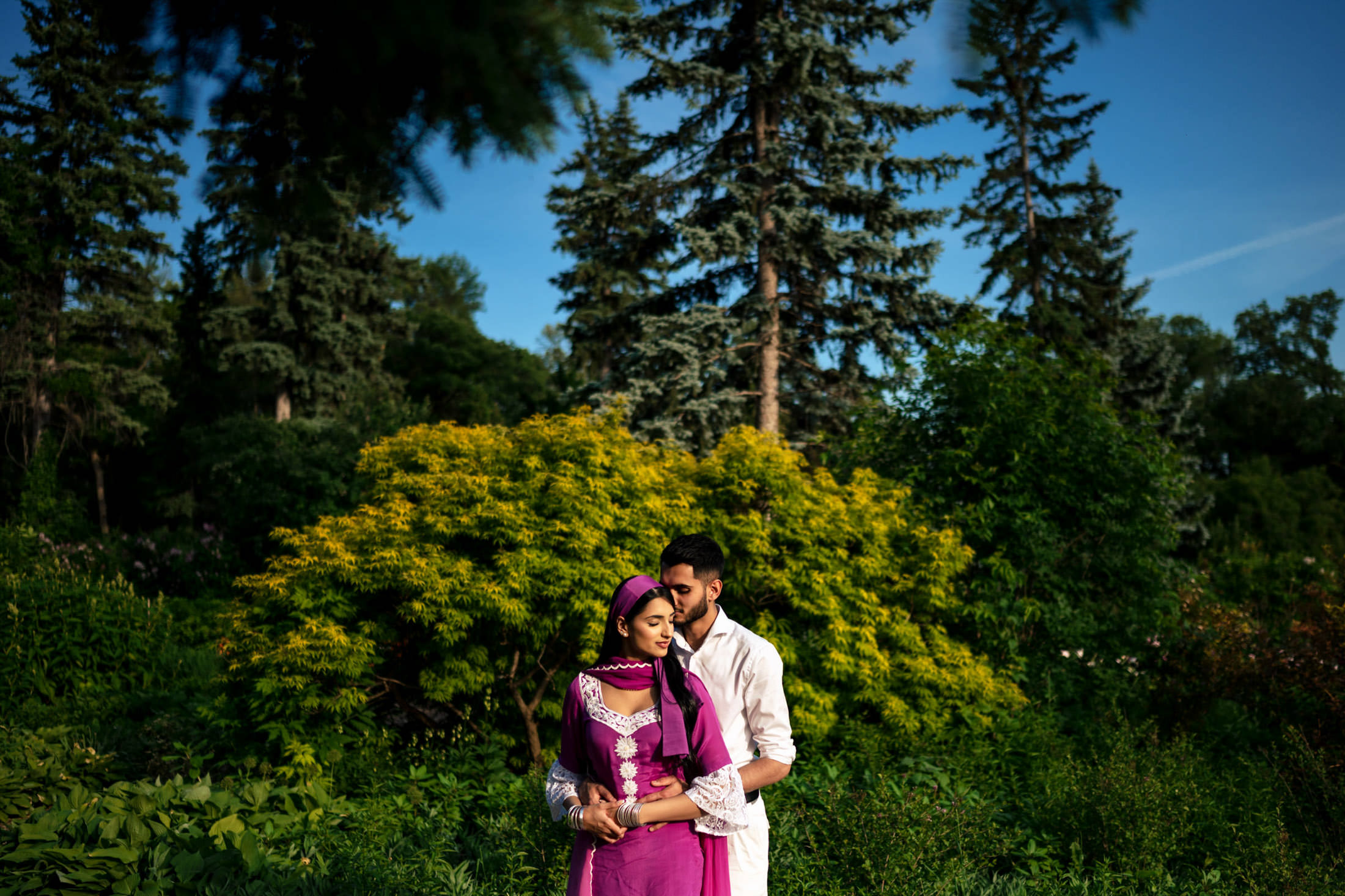 Couple embracing in a lush forest, celebrating their engagement among tall trees.