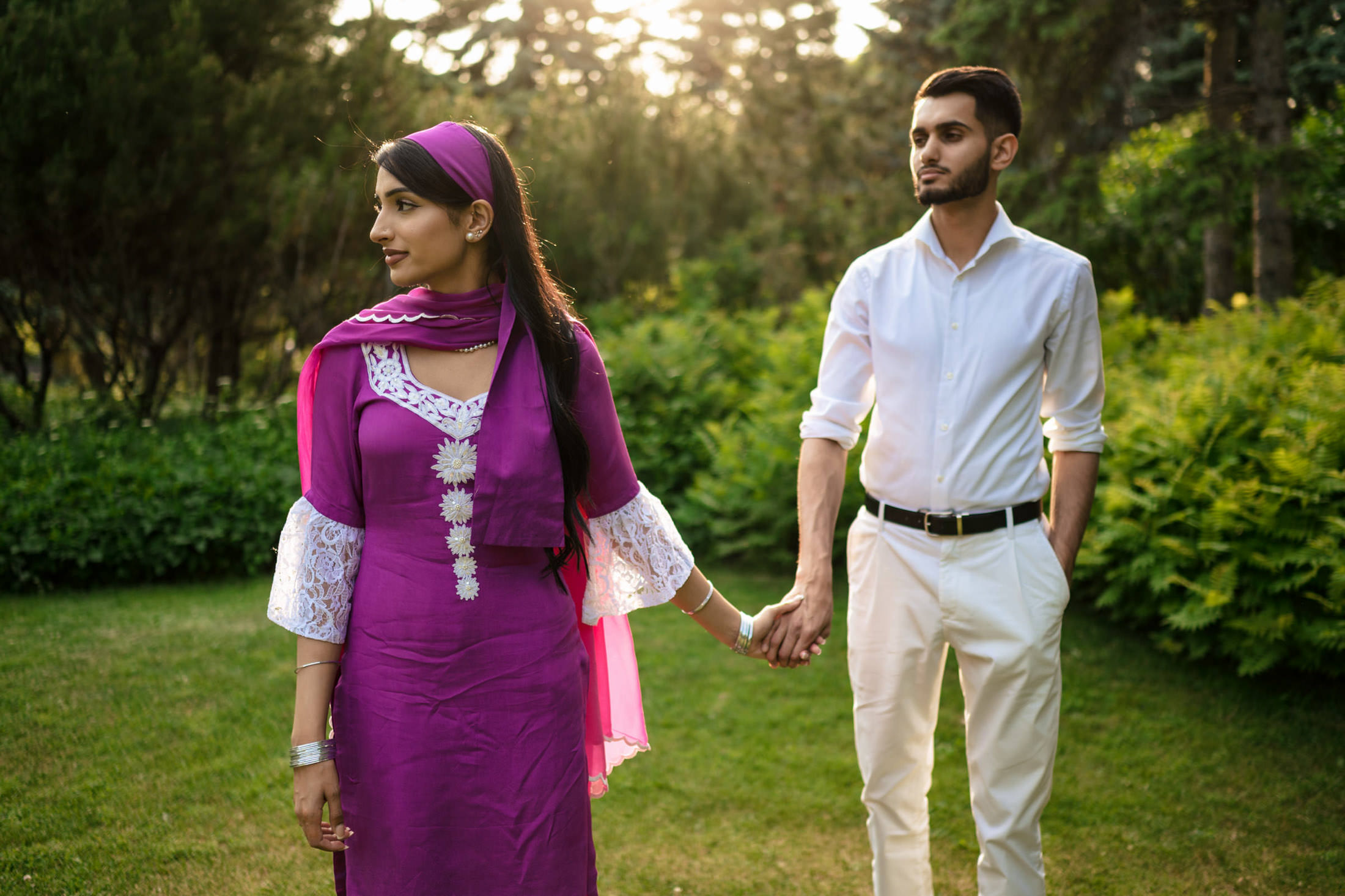 Engagement at home: Couple holding hands, woman in purple dress, man in white shirt, in a garden.