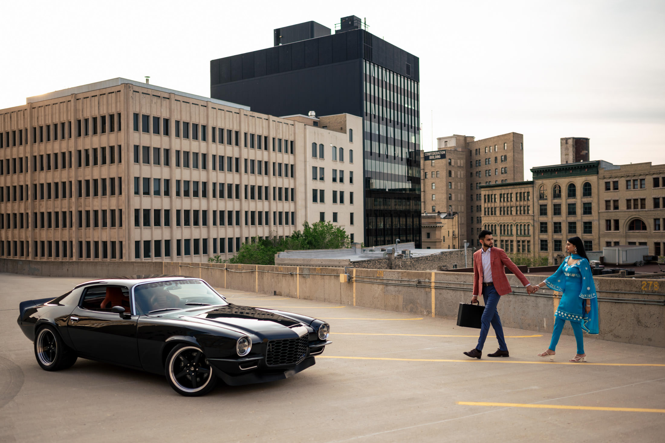 A couple walks hand-in-hand towards a black classic car, marking their engagement.