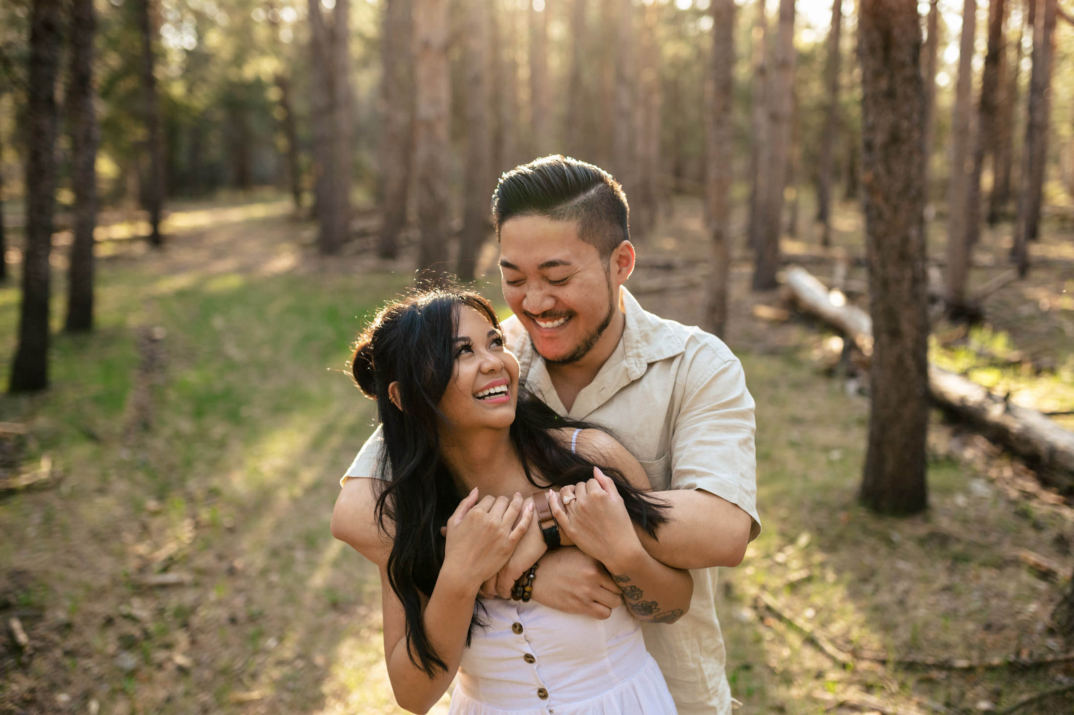 Couple joyfully embracing with their dog in a sunlit forest clearing.