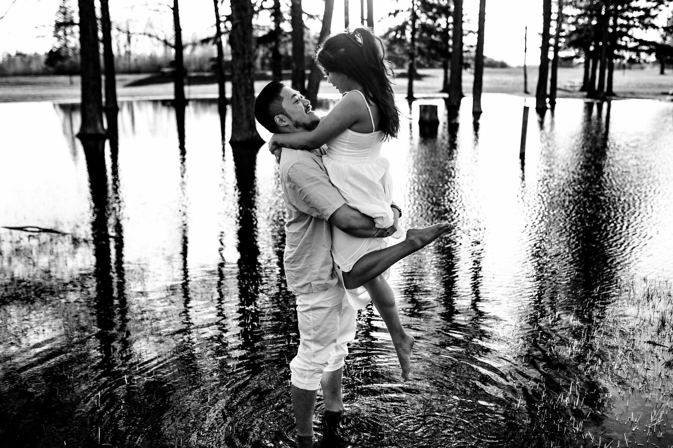 A couple joyfully embracing, while their dog frolics in a flooded woodland area.
