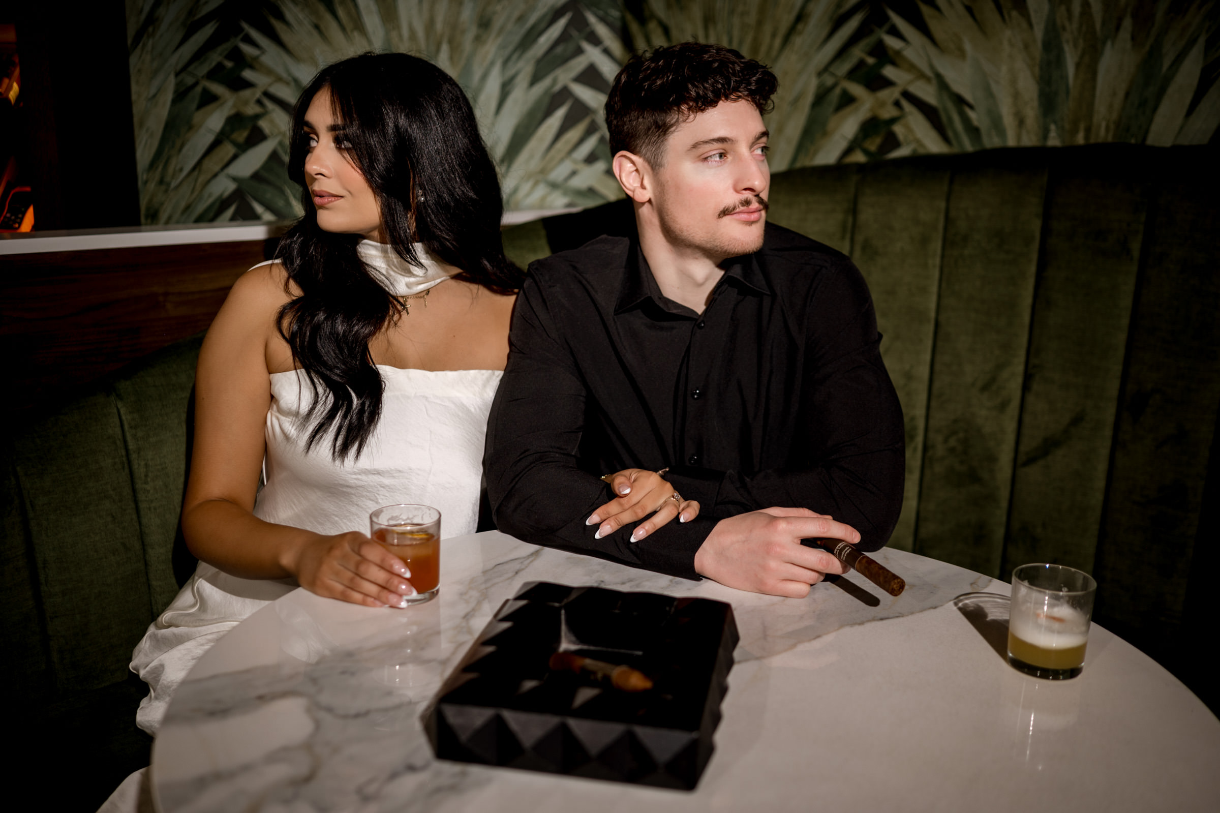 A couple enjoys drinks and cigars in a dimly lit Winnipeg engagement setting.