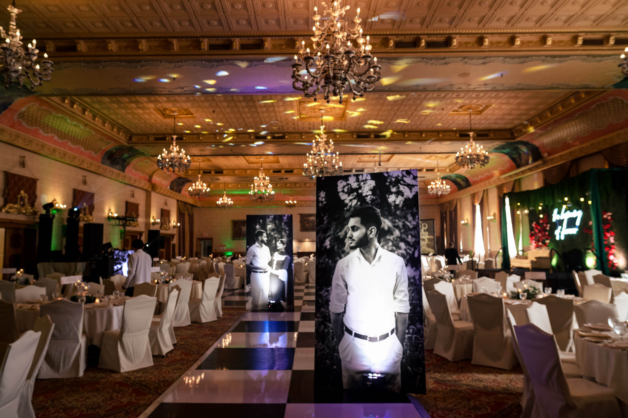 Elegant Winnipeg wedding hall with chandeliers, white chairs, and black-and-white portraits.