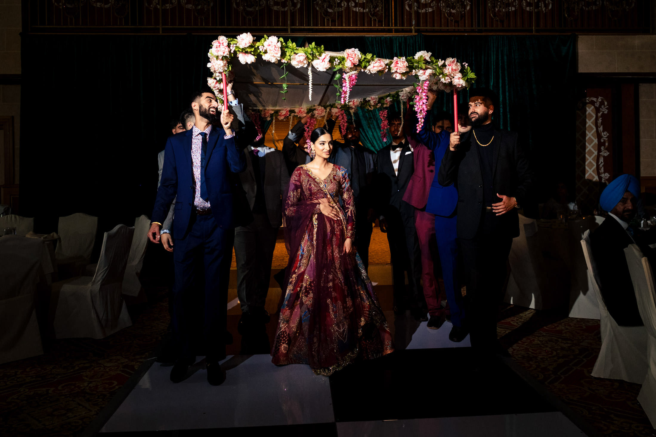 Bride walking under floral canopy with four attendants in formal attire at Winnipeg wedding.