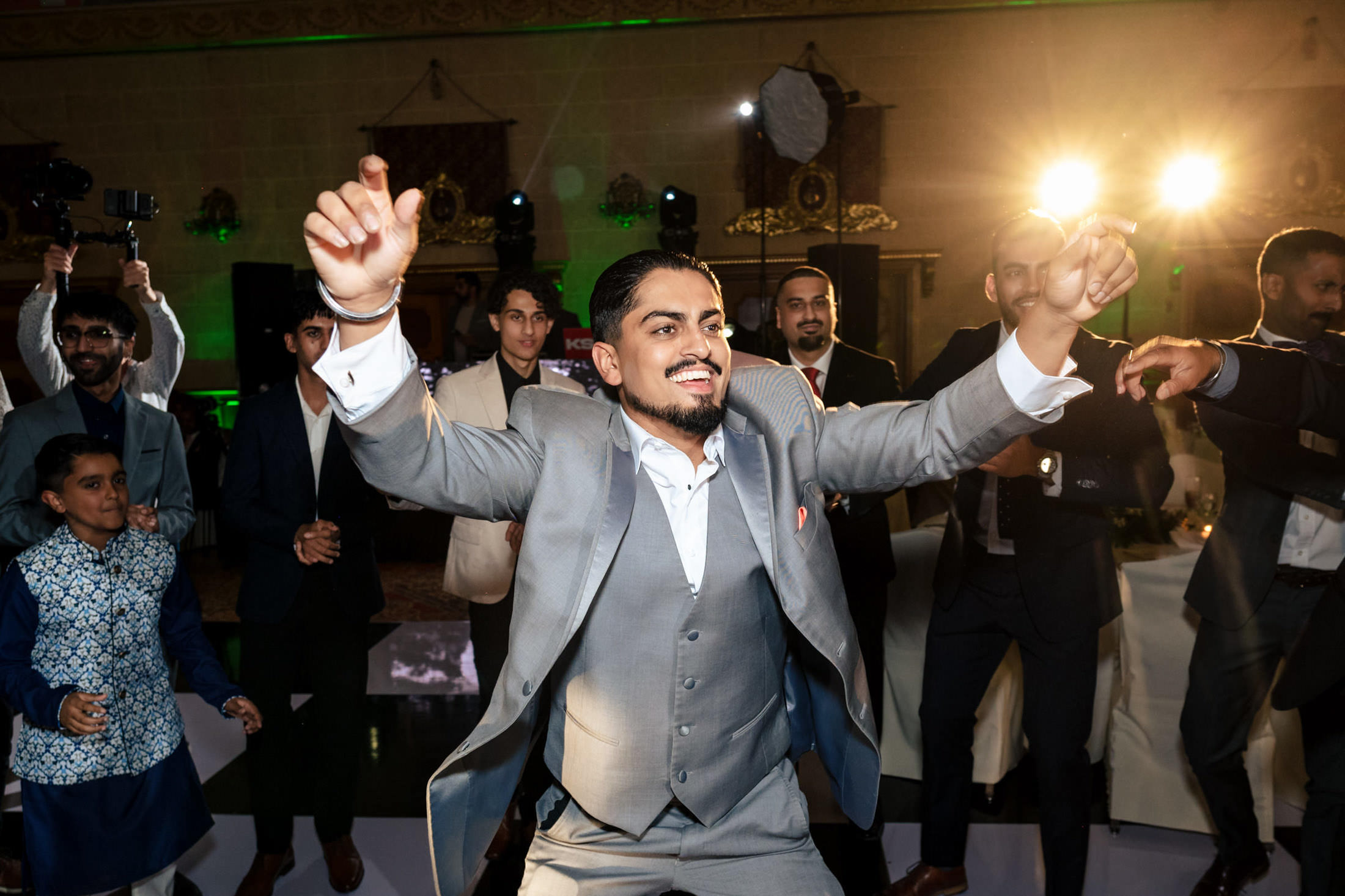 Man in a gray suit energetically dancing at a lively Winnipeg wedding celebration.