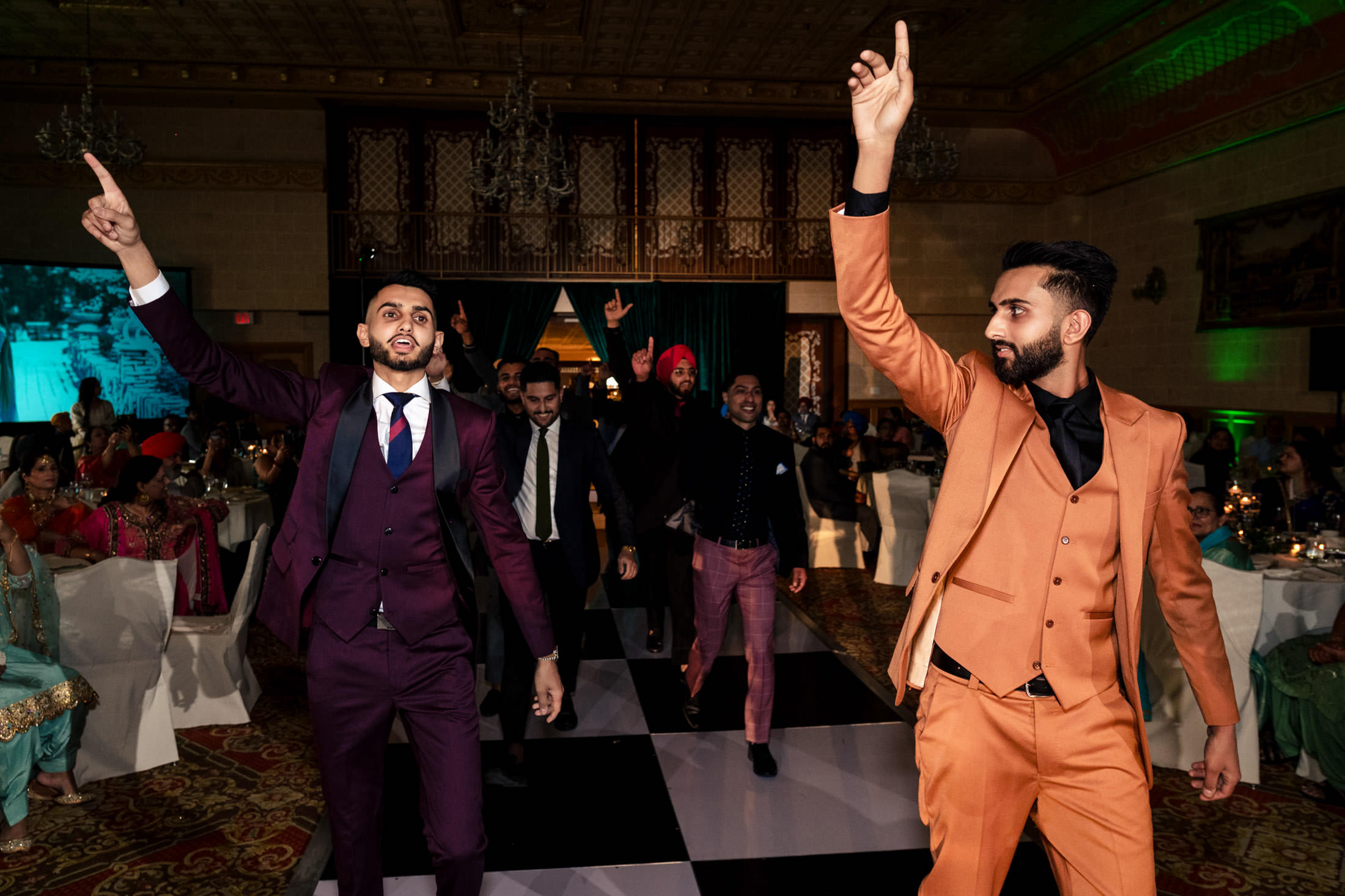Men in formal suits dance energetically at a lively Winnipeg wedding celebration.
