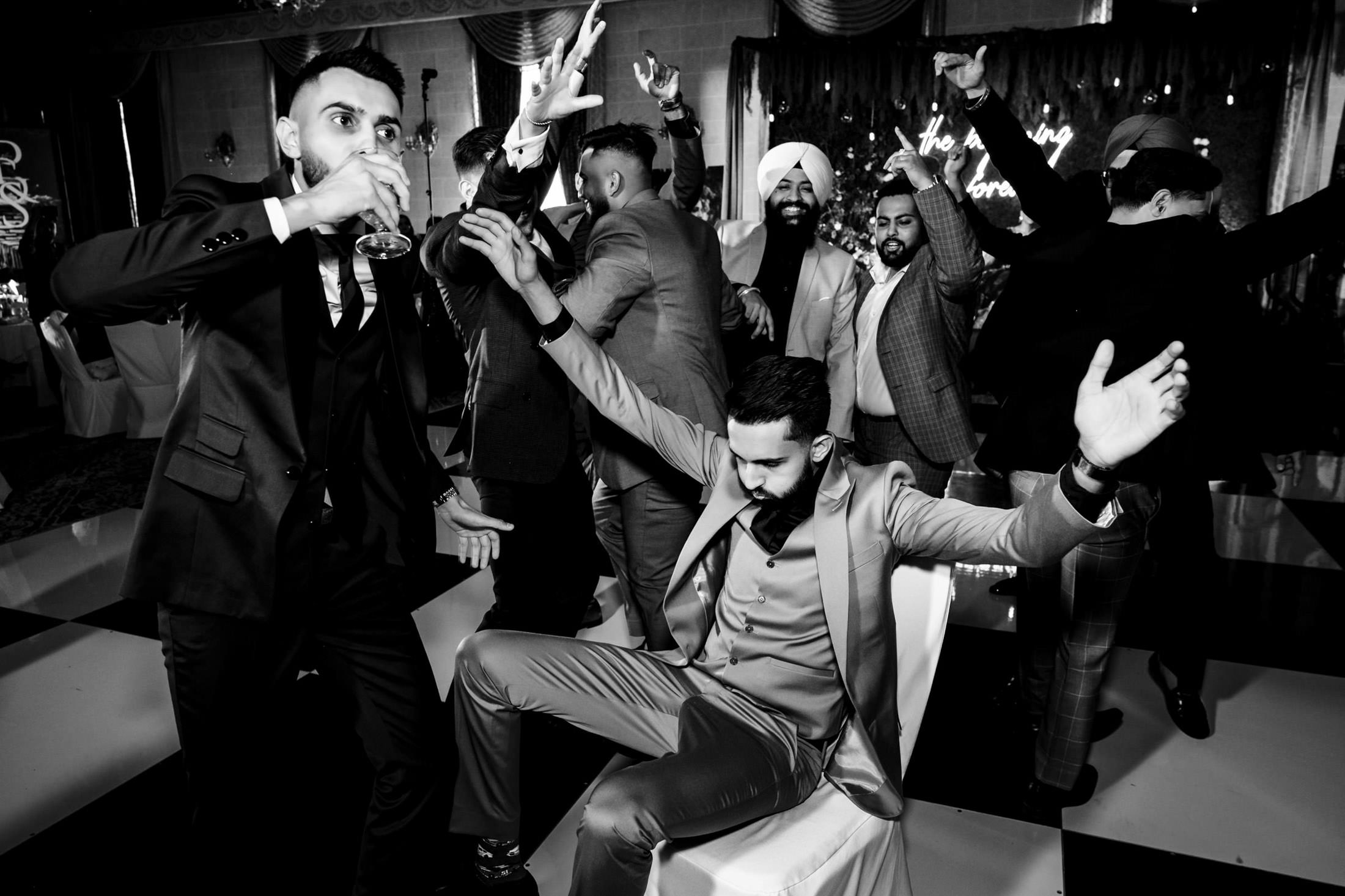 Group of men energetically dancing at a Winnipeg wedding; one guy sits, arms raised.