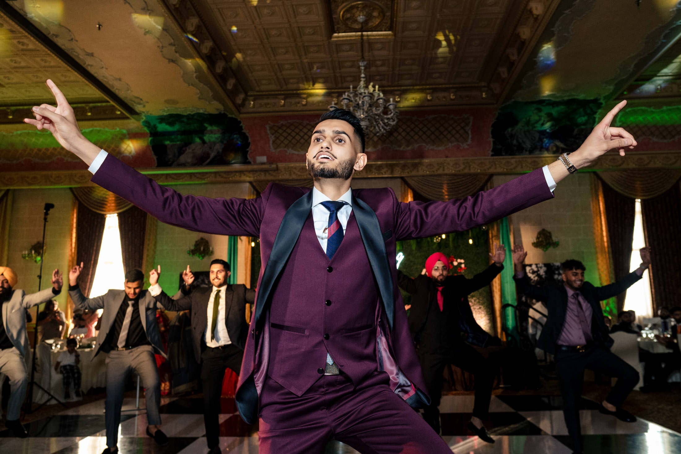 Man in maroon suit dancing energetically at a lively Winnipeg wedding celebration.