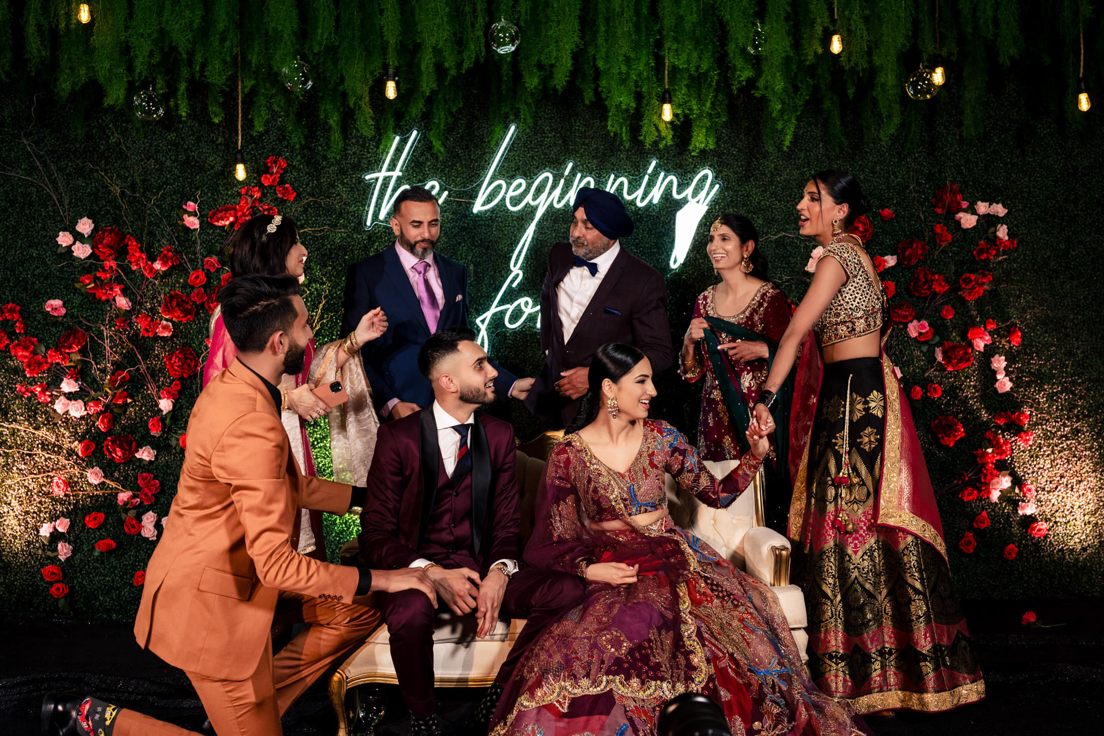 People in vibrant attire celebrate a Winnipeg wedding, surrounded by red flowers and foliage.