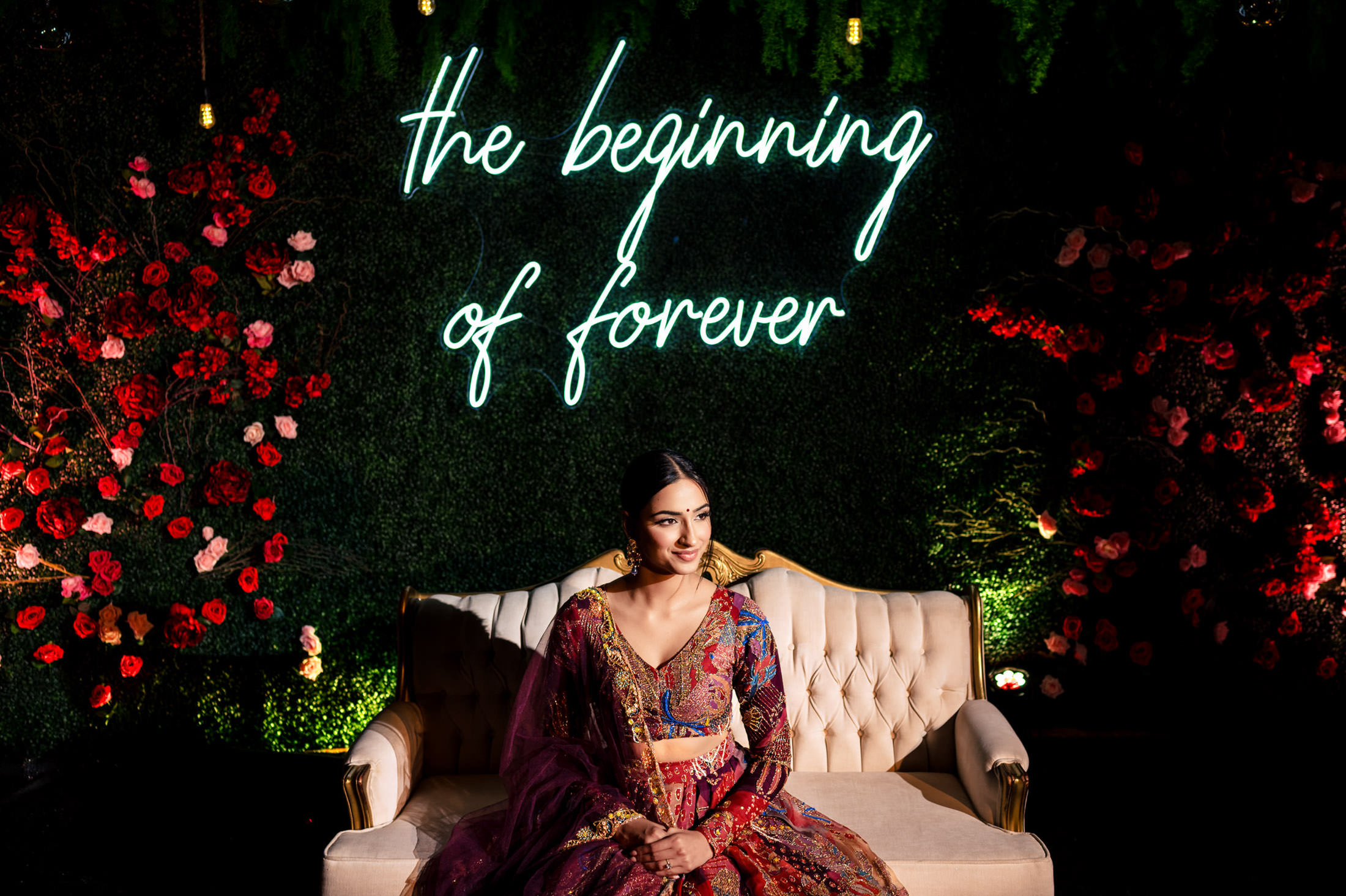 A woman in a colorful outfit sits on a couch under a neon sign at a Winnipeg wedding.