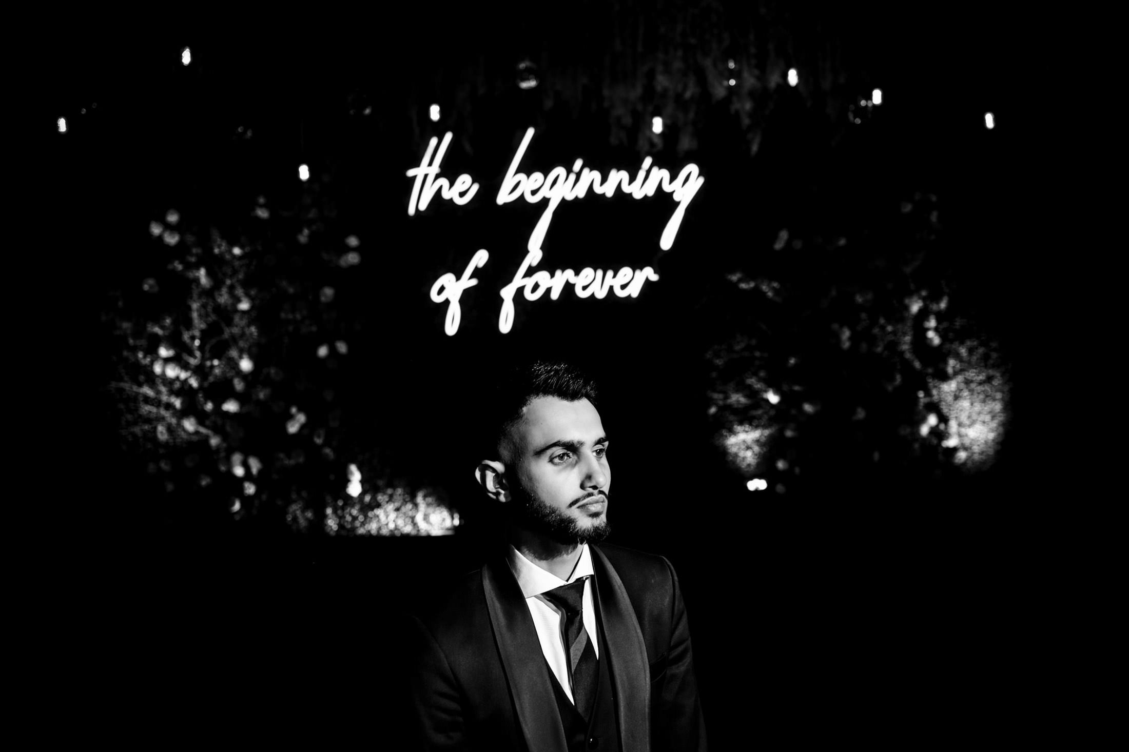 Man in a suit stands under sign reading "the beginning of forever" at Winnipeg wedding.