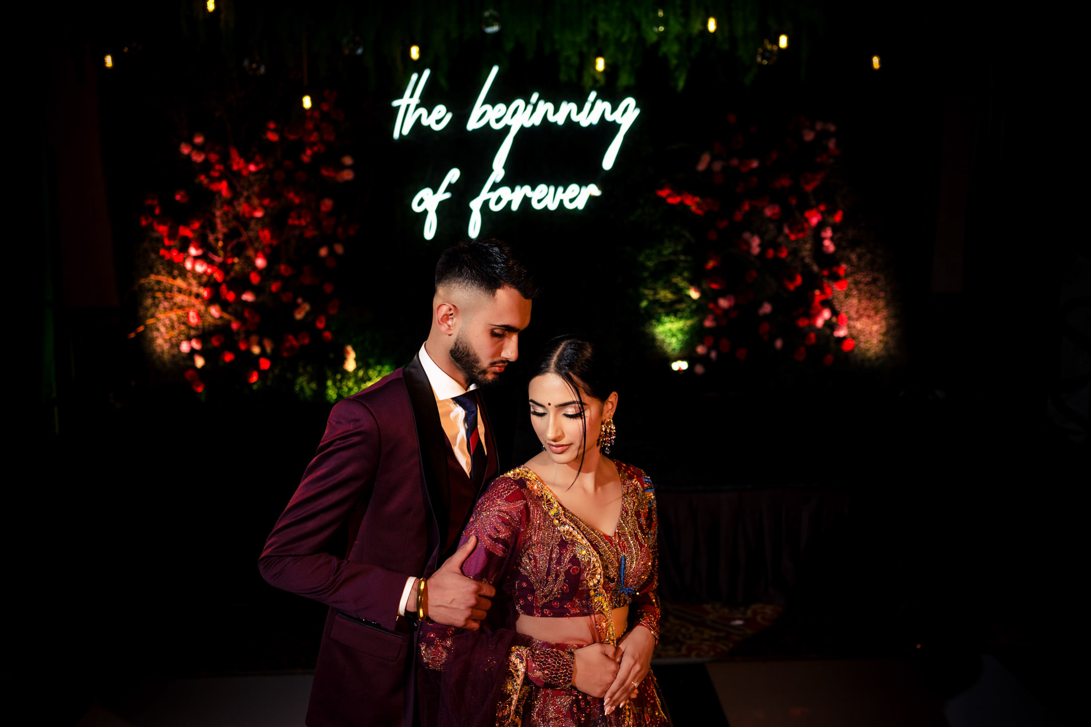A couple in formal attire dances under a neon "the beginning of forever" at their Winnipeg wedding.