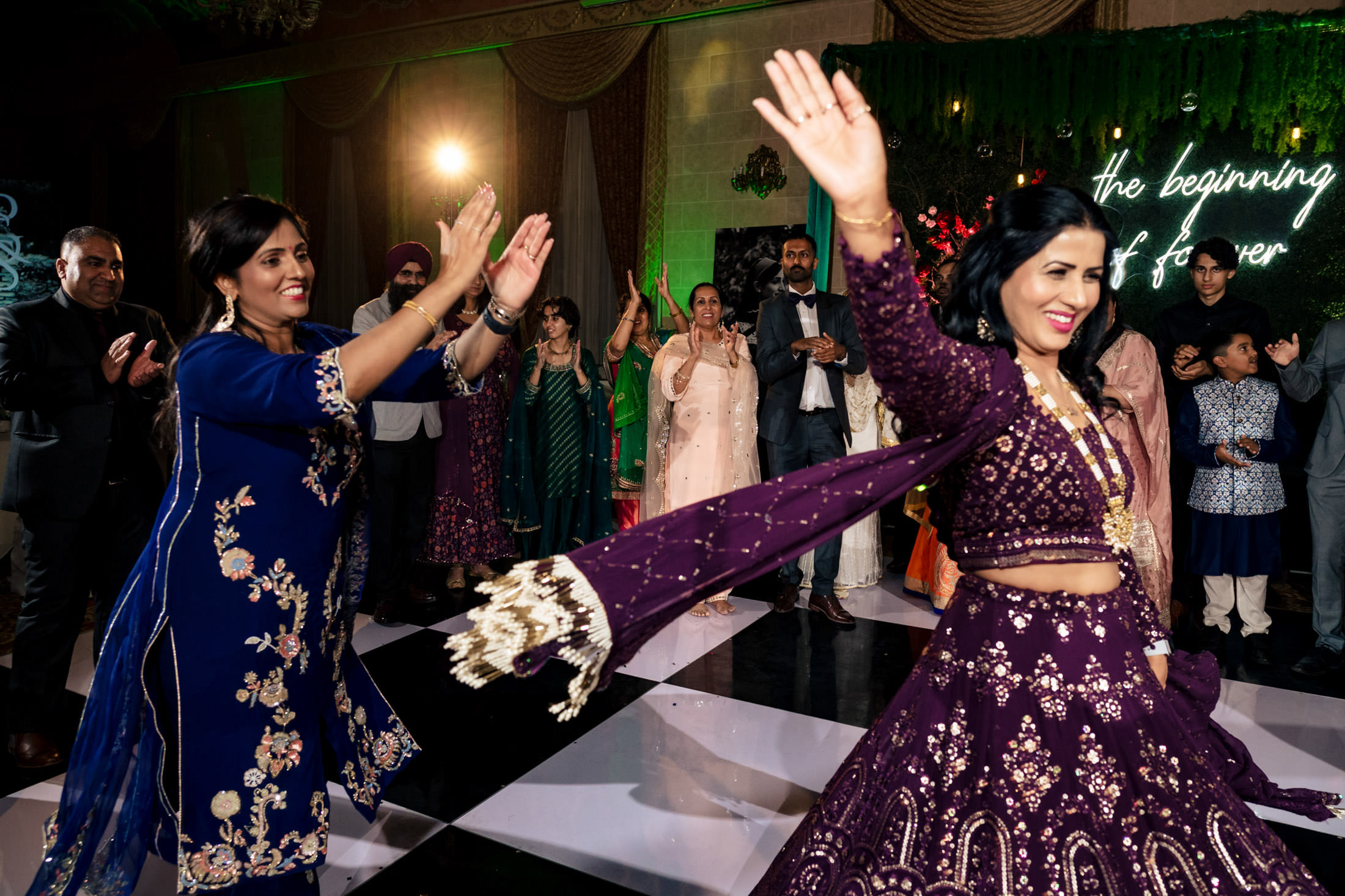 Two women joyfully dancing in ornate purple gowns at a festive Winnipeg wedding.