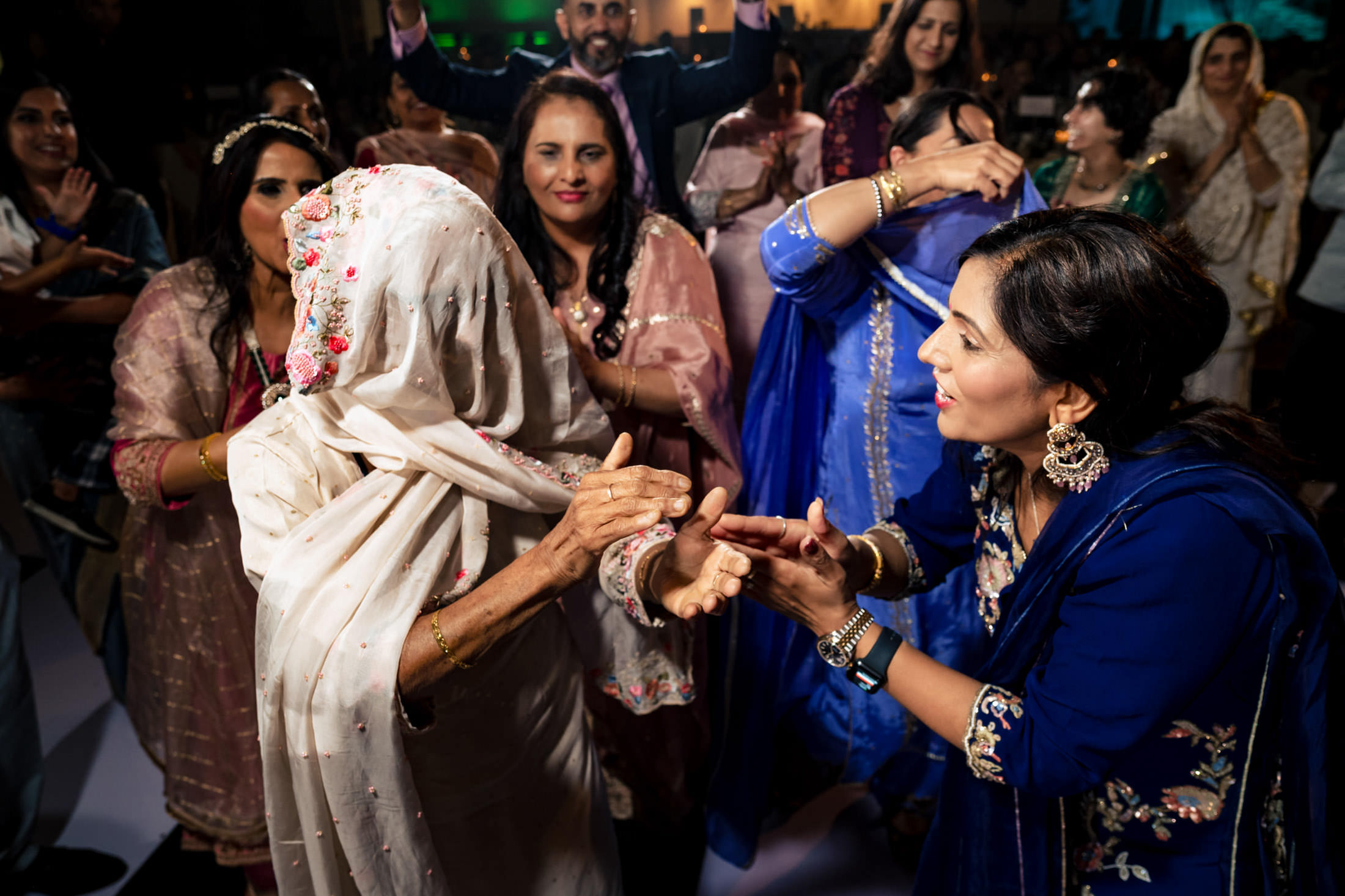 A joyful group of women in colorful attire dance together at a lively Winnipeg wedding.