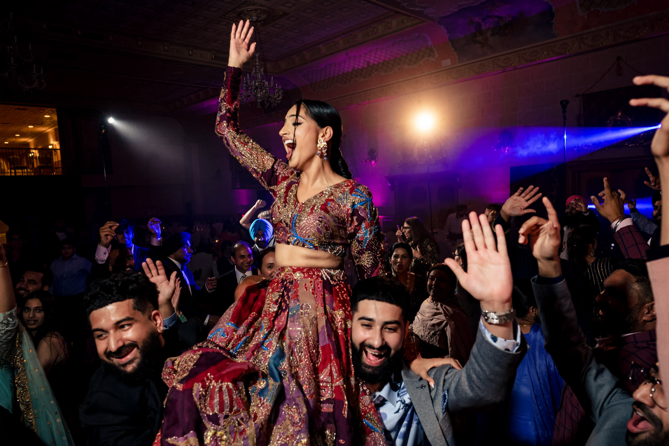 A joyful woman in a colorful dress is lifted up at a lively Winnipeg wedding.