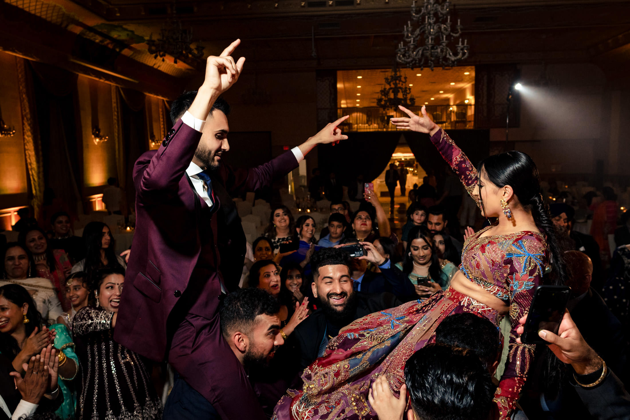 People celebrating at a lively Winnipeg wedding, with one woman lifted on chairs.