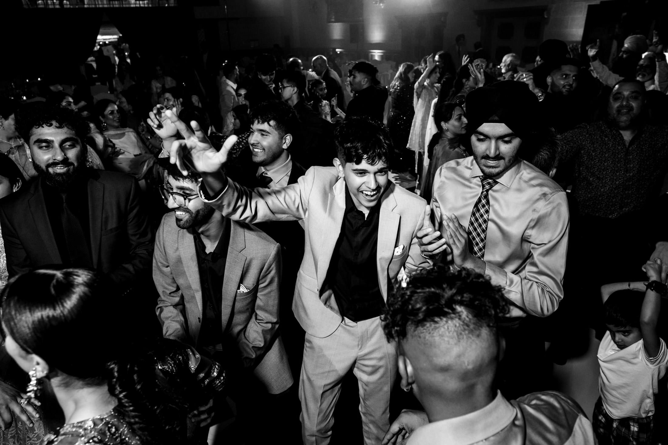 People dancing energetically at a Winnipeg wedding, with joyful expressions and raised hands.