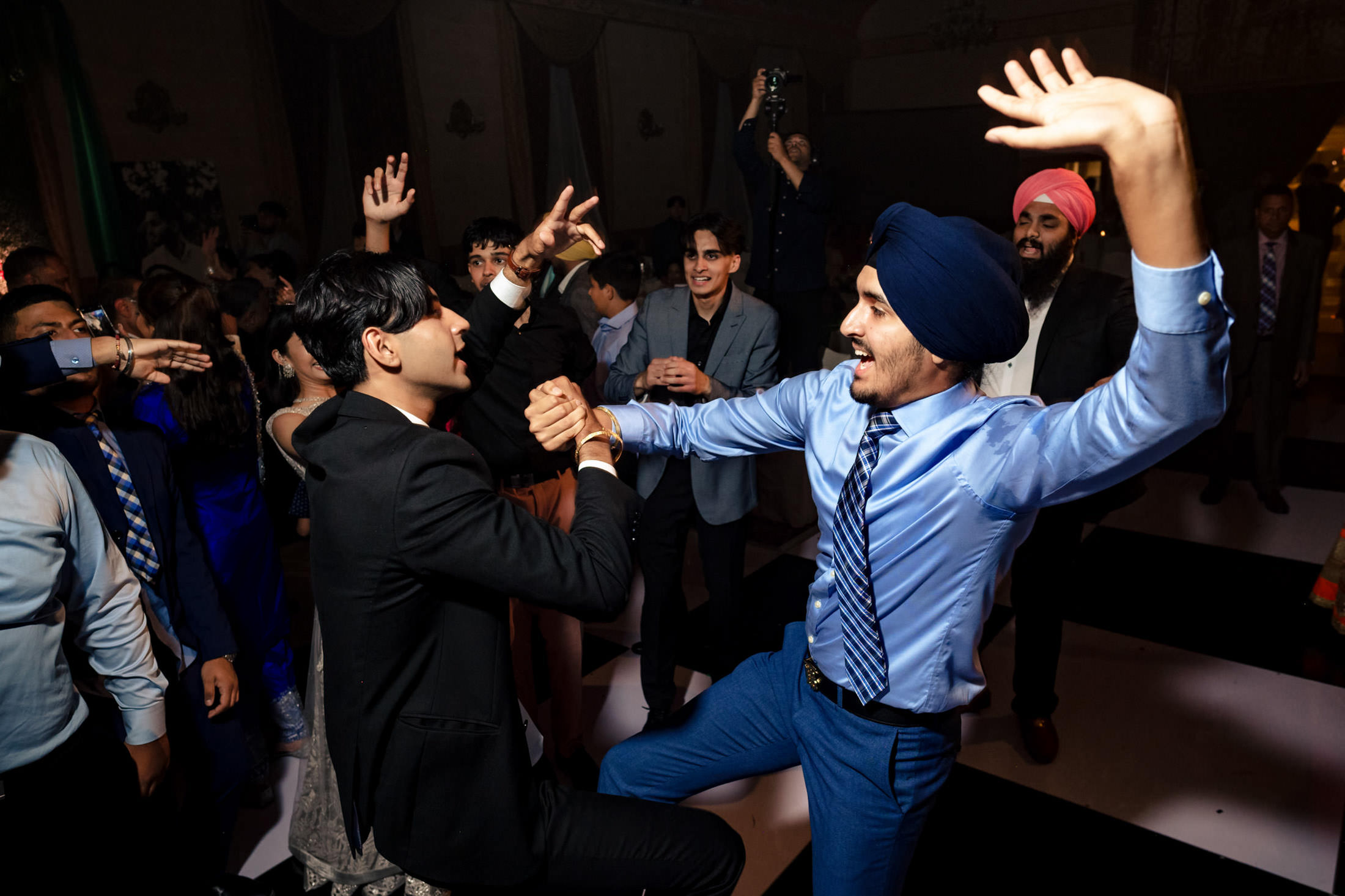 People dancing energetically at a Winnipeg wedding, two men in suits holding hands in the foreground.