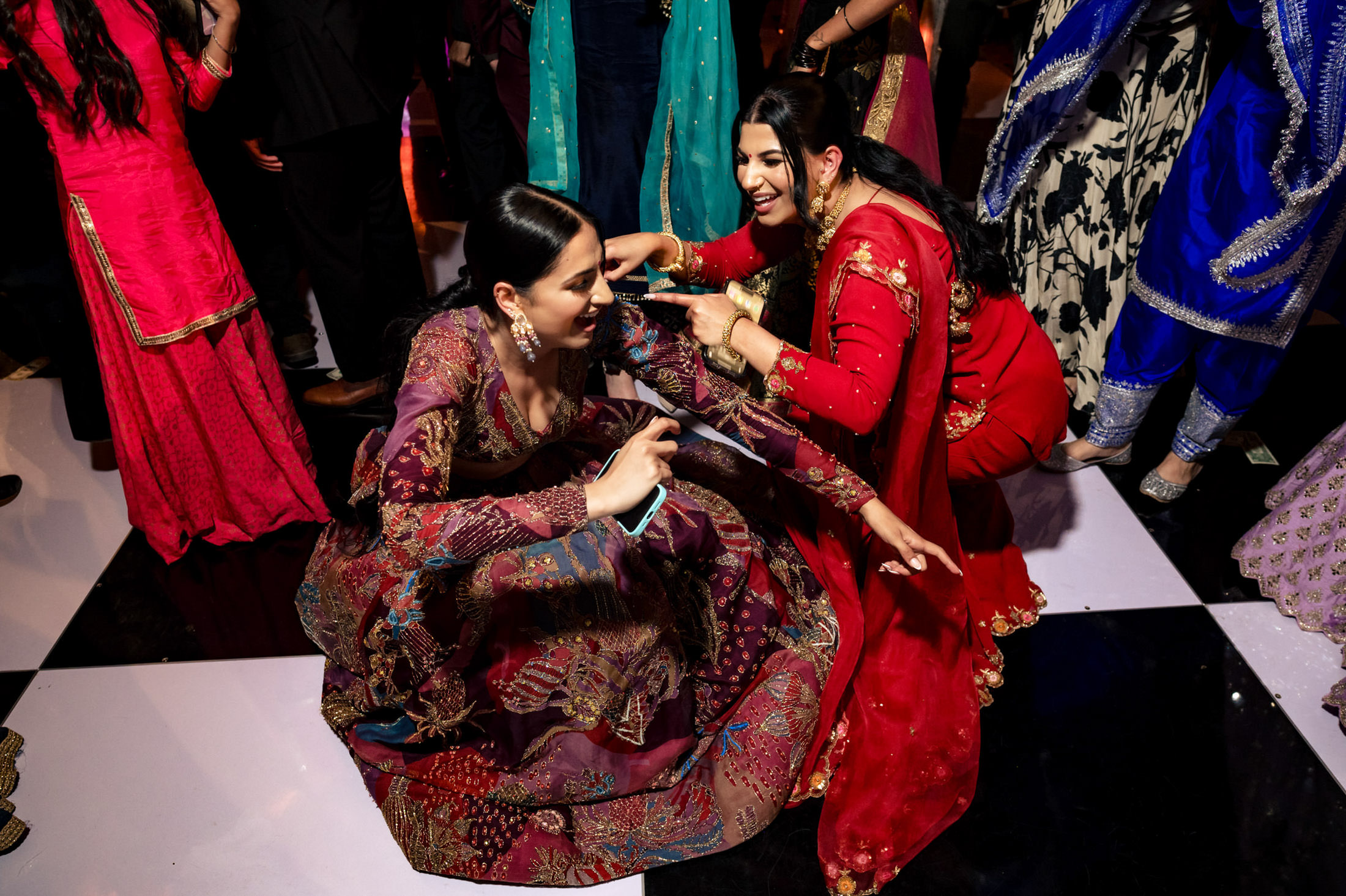 Women in colorful attire dance joyfully at a lively Winnipeg wedding indoors.