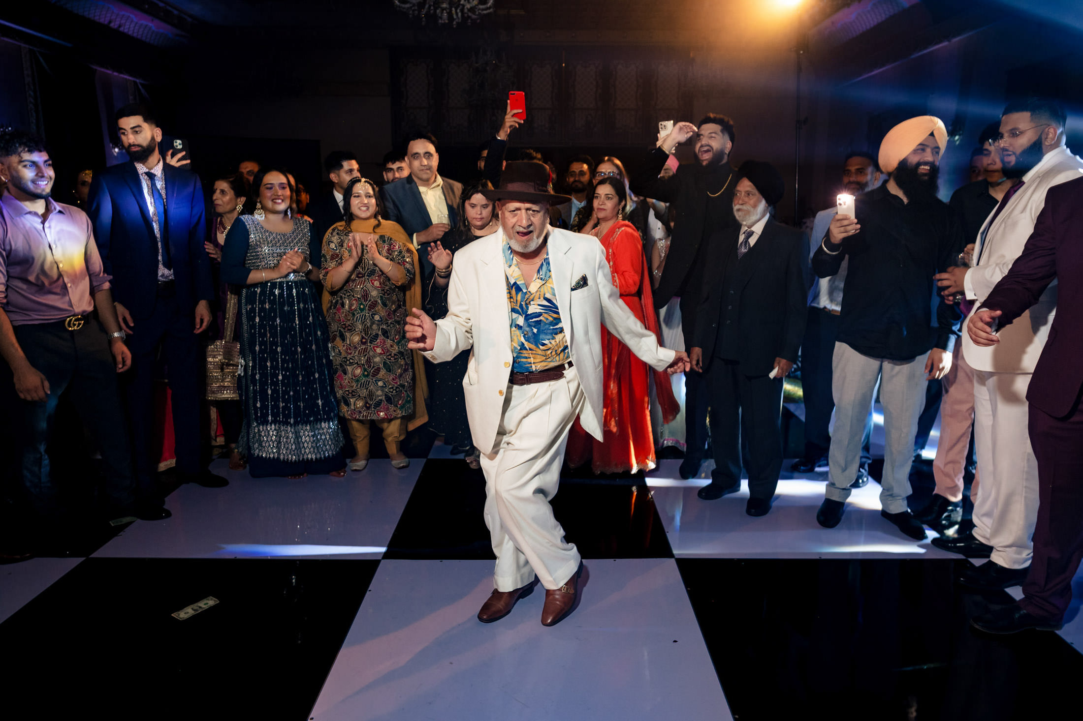 At a Winnipeg wedding, an elderly man dances in a white suit on a checkered floor.