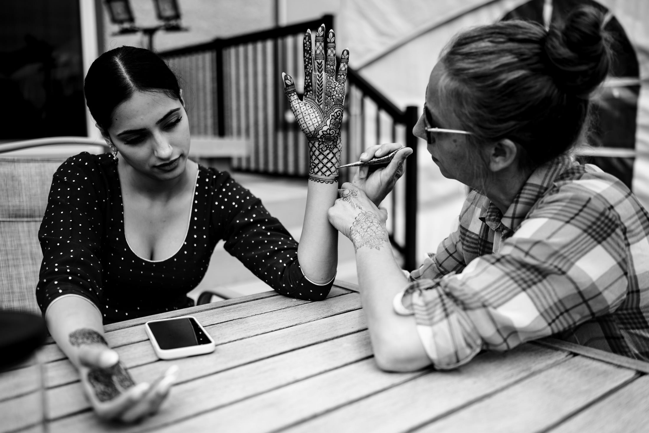 Two women at a table, one applying henna for a Winnipeg wedding on the other's hand.