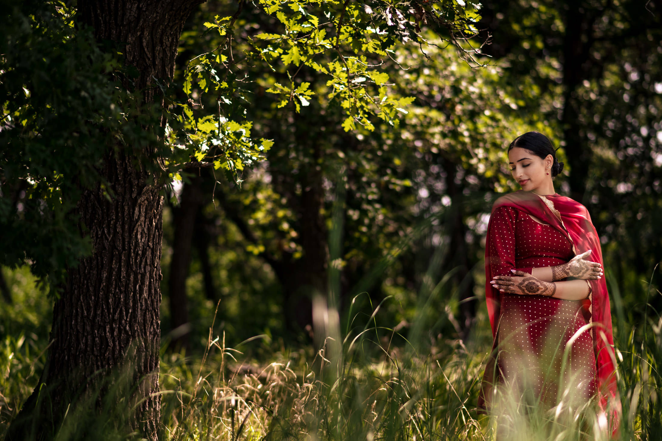 Woman in red dress stands under a tree, capturing a Winnipeg wedding moment.