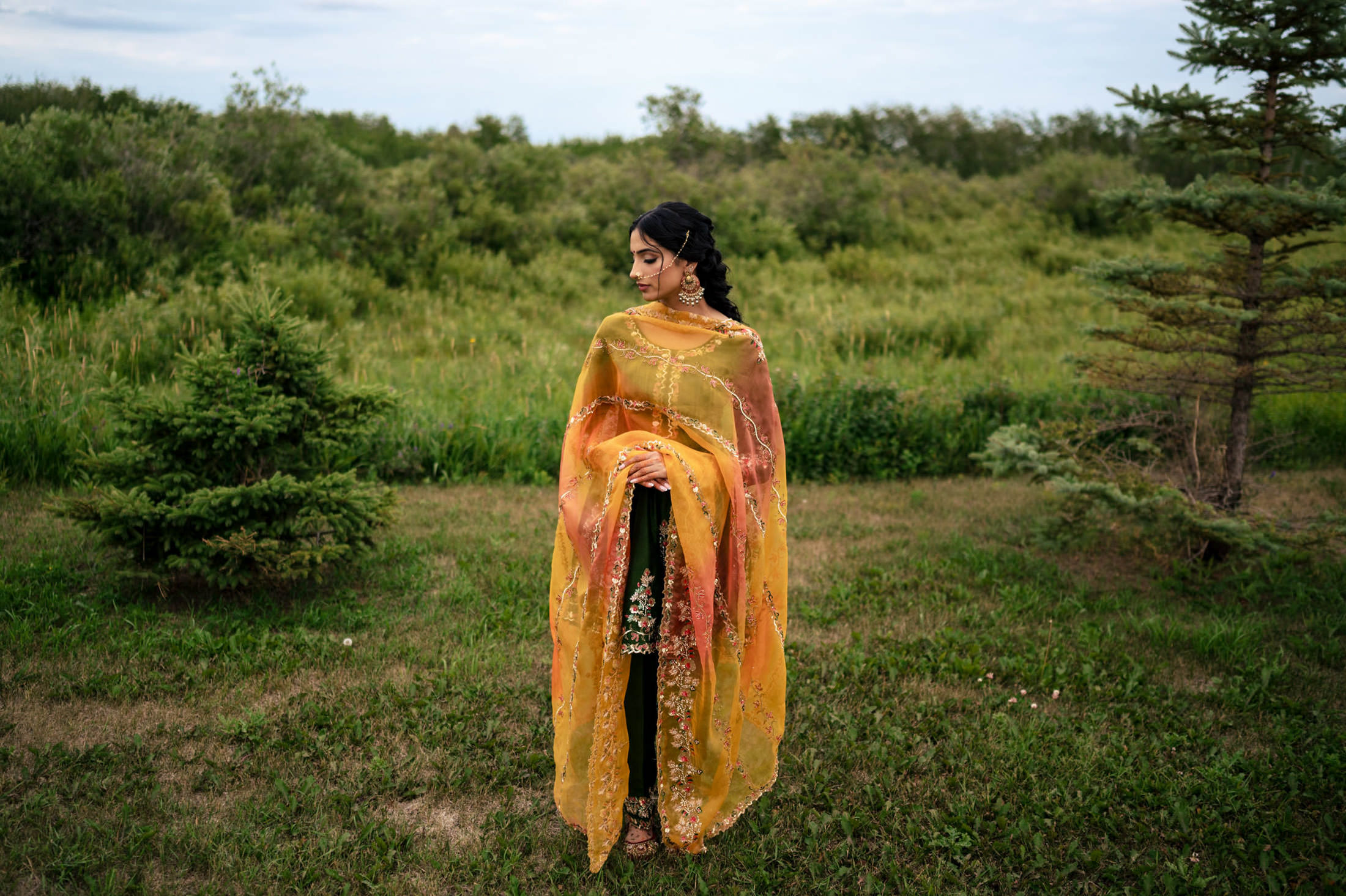 Person in colorful traditional attire stands in a green field at a Winnipeg wedding.