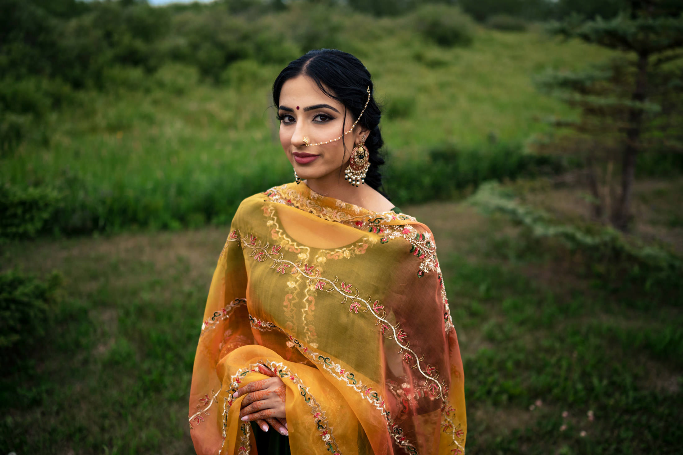 A person in an orange sari stands in a grassy field at a Winnipeg wedding.