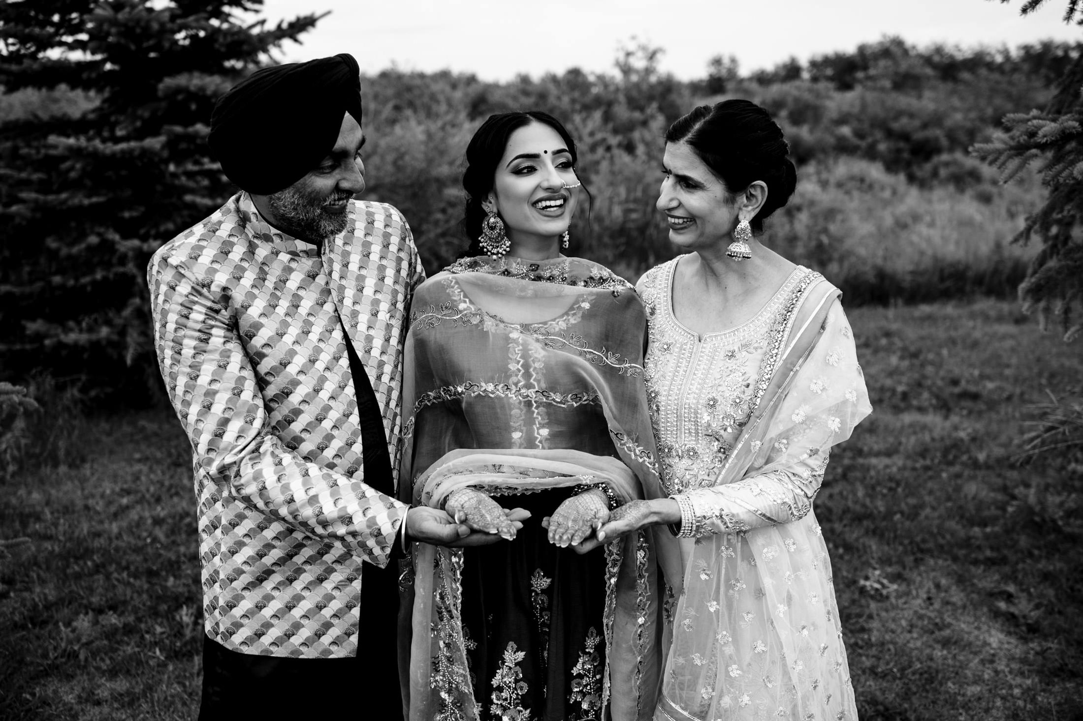 Three people in traditional attire, smiling and holding hands at a Winnipeg wedding.