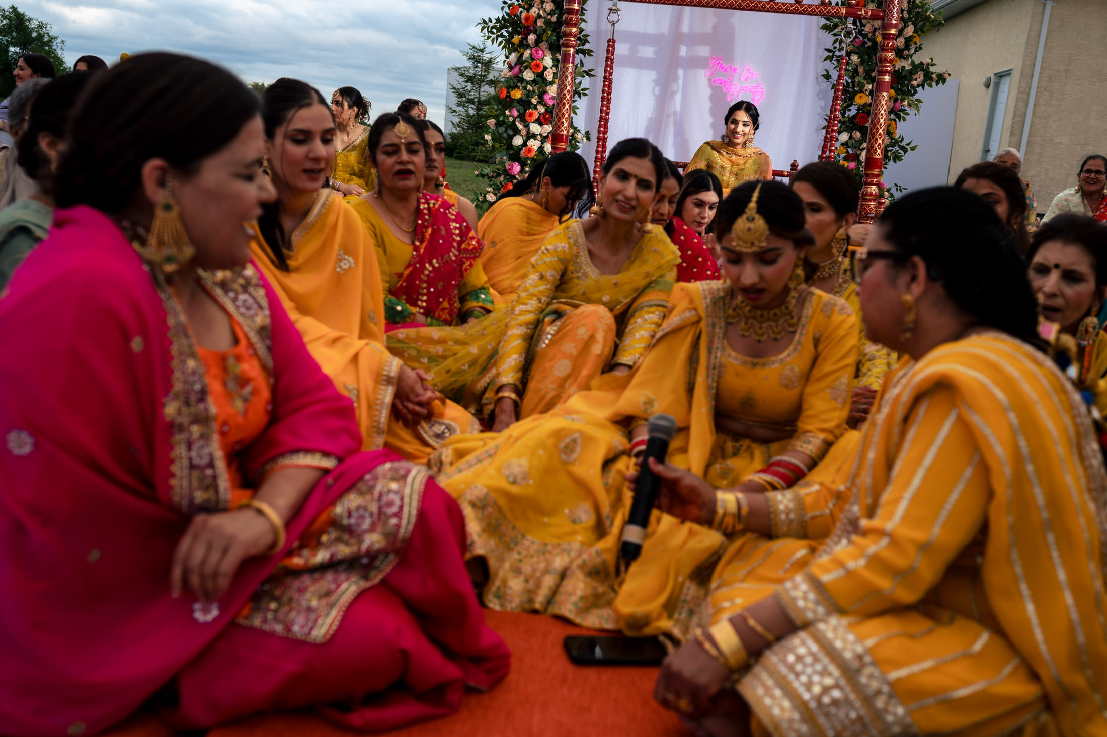 Women in colorful attire gather with a microphone at a vibrant Winnipeg wedding event.