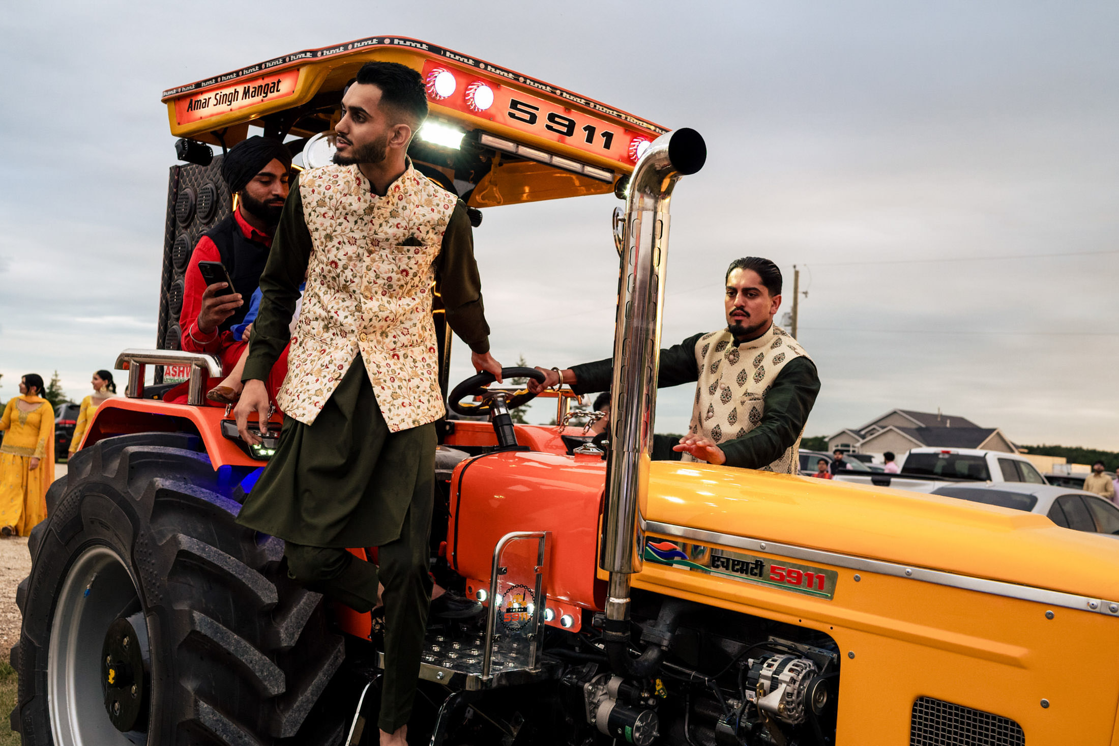 Three men in traditional attire pose by an orange tractor at a Winnipeg wedding.