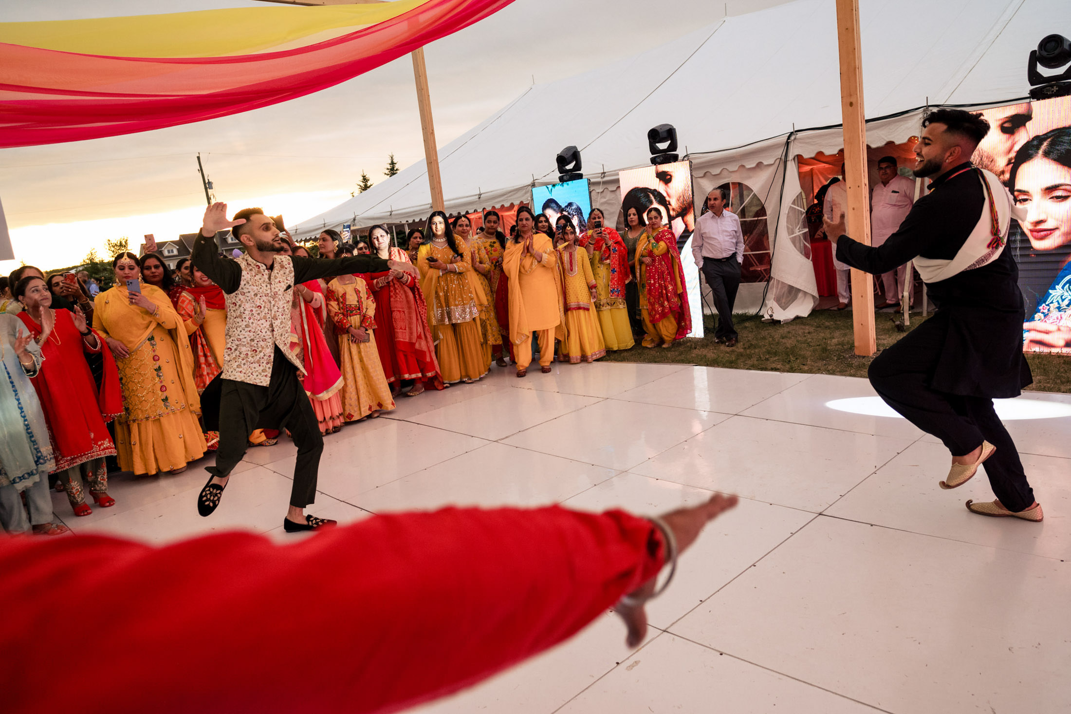 Two people dancing energetically at a Winnipeg wedding under a colorful tent canopy.