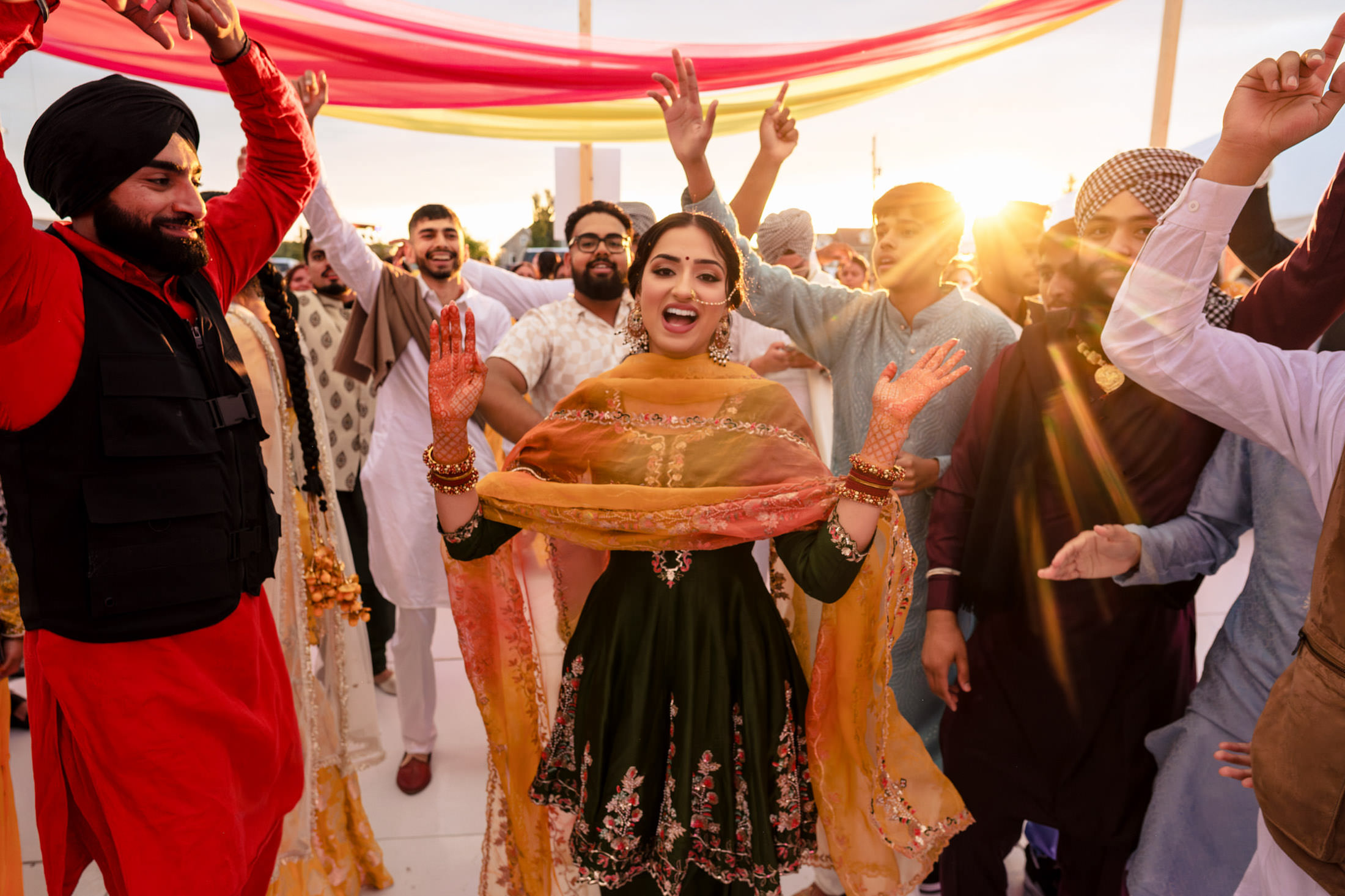 Group celebrating a Winnipeg wedding with dancing, colorful clothing, and vibrant drapes at sunset.