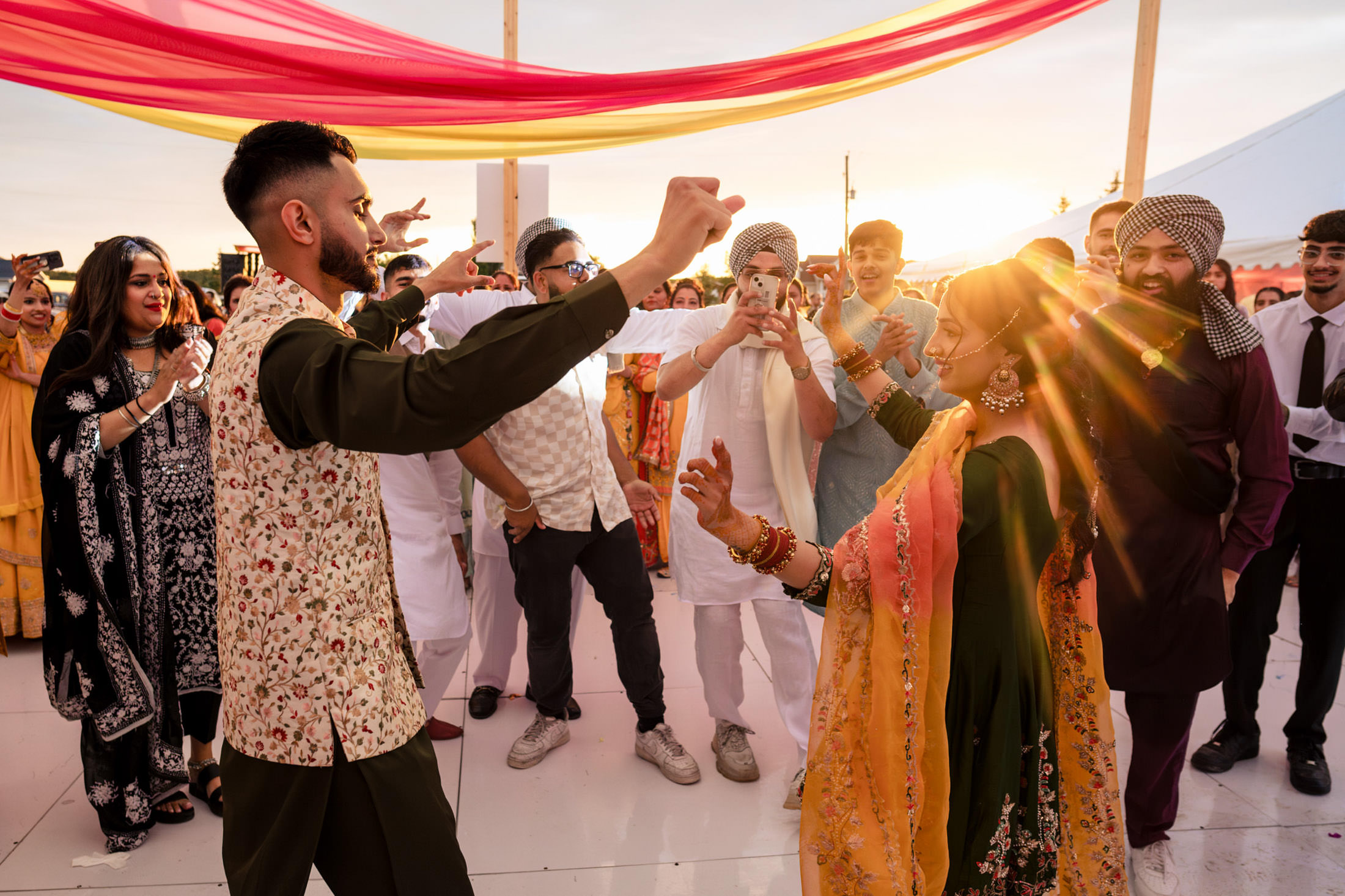 People dancing joyfully at a Winnipeg wedding, colorful drapes and a setting sun in the background.