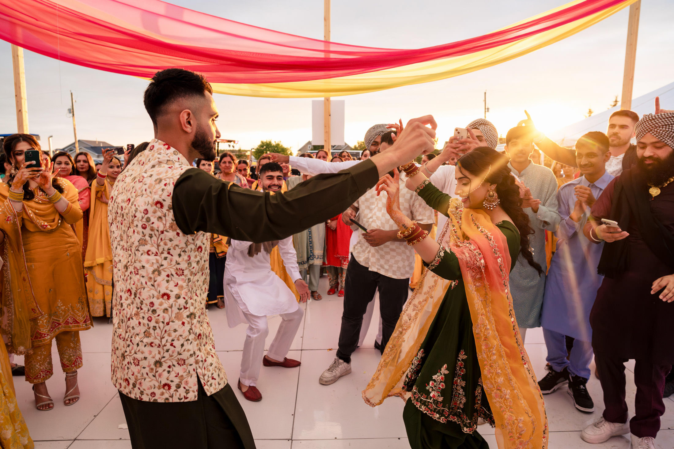 A joyful couple dances outdoors at sunset during a colorful Winnipeg wedding.