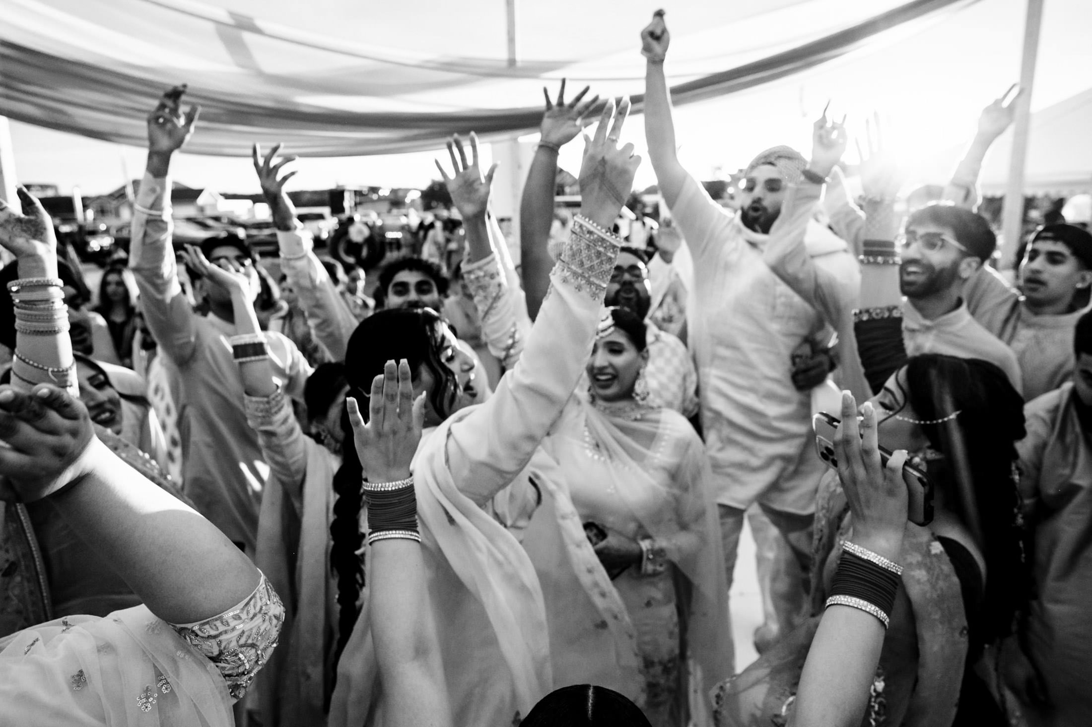 People joyfully dancing at a Winnipeg wedding, hands raised, in traditional attire.