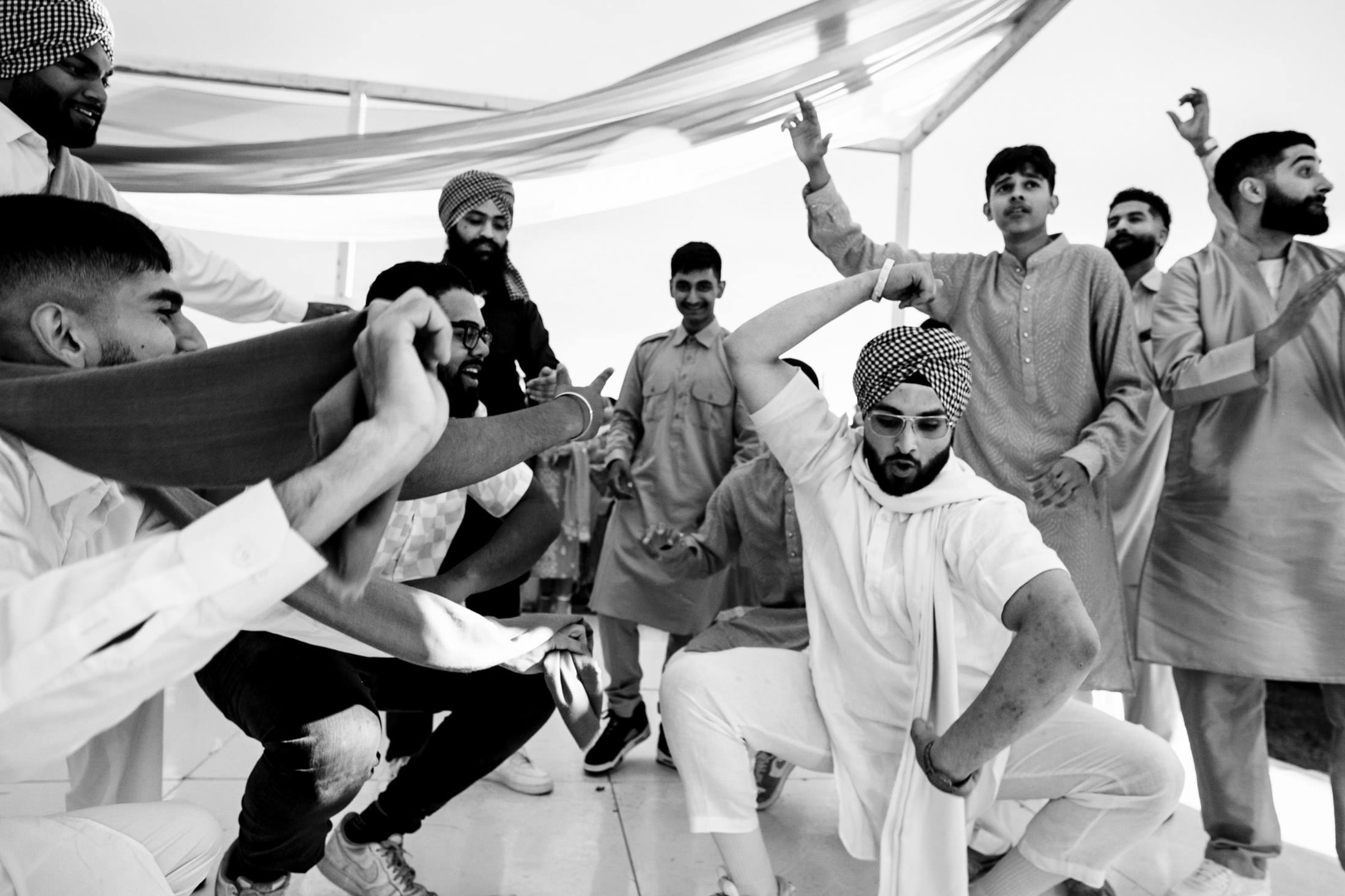 Group of people dancing energetically in traditional clothing at a Winnipeg wedding.